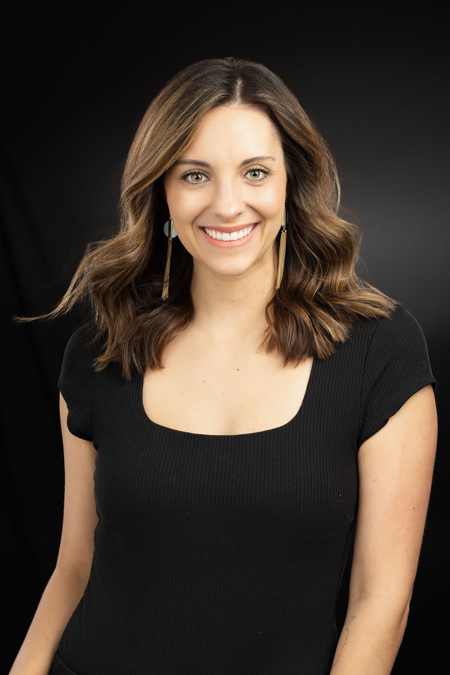 Professional headshot of woman with shoulder-length wavy hair wearing black scoop neck top.