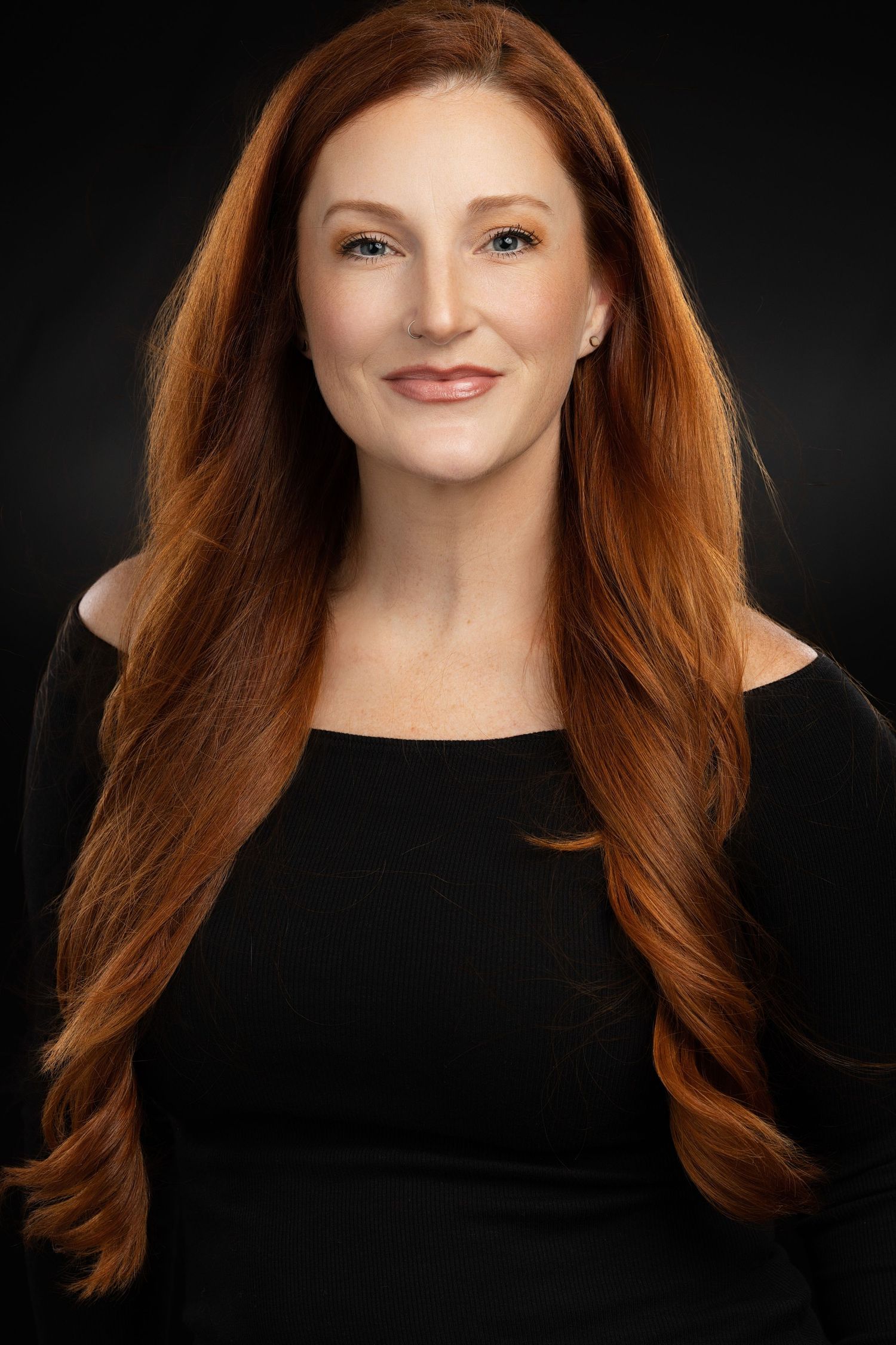 Professional portrait of woman with flowing auburn hair wearing black top against dark background.