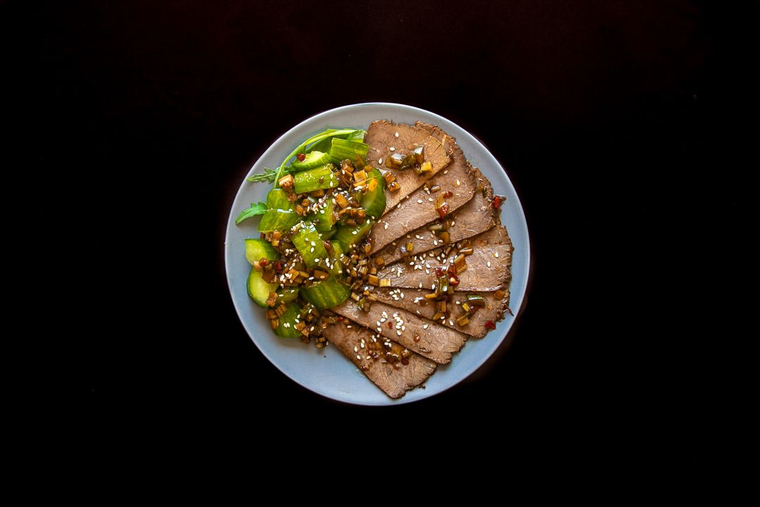 Grilled meat dish with vegetables plated on white dishes against dark background.
