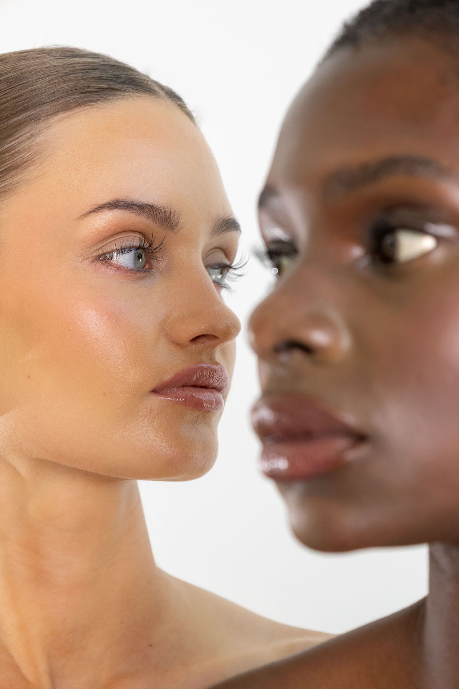 Close-up portrait of two diverse women with glowing skin and lifted lashes side by side.
