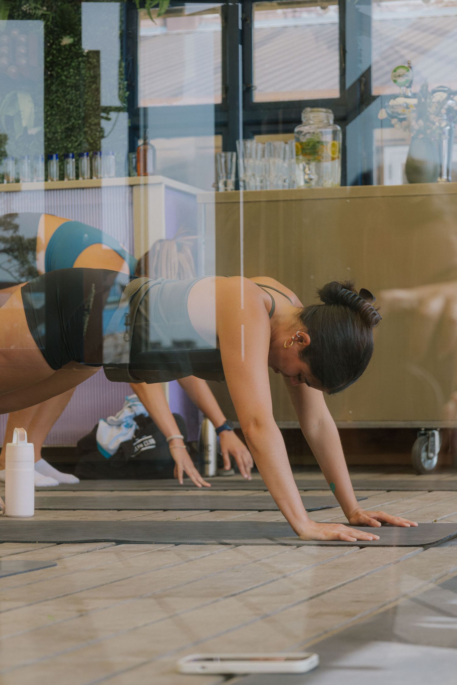 People practicing yoga poses on mats in sunlit studio space.