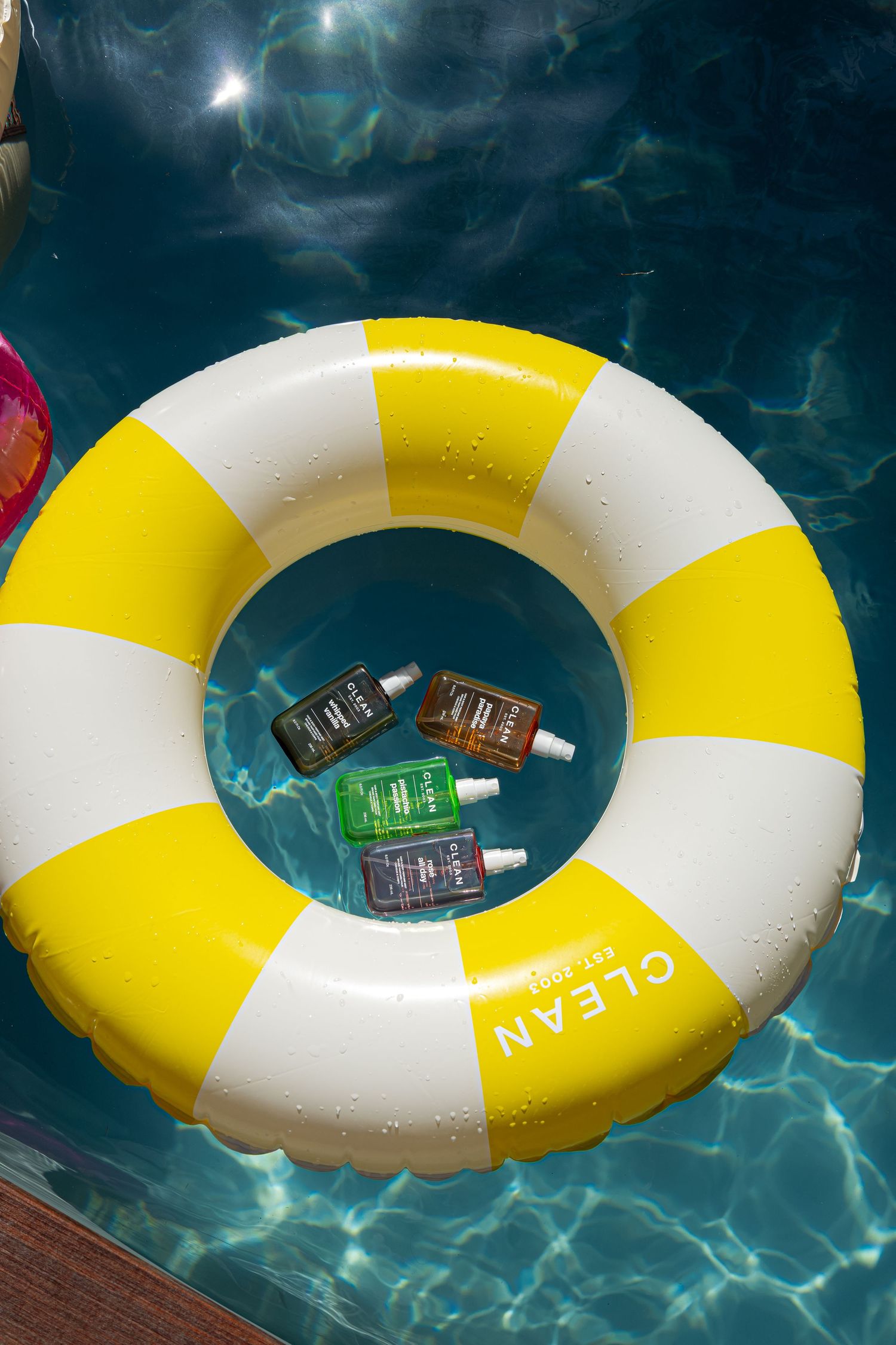 Yellow and white striped inflatable pool ring floating in turquoise water with Clean beauty product bottles inside.
