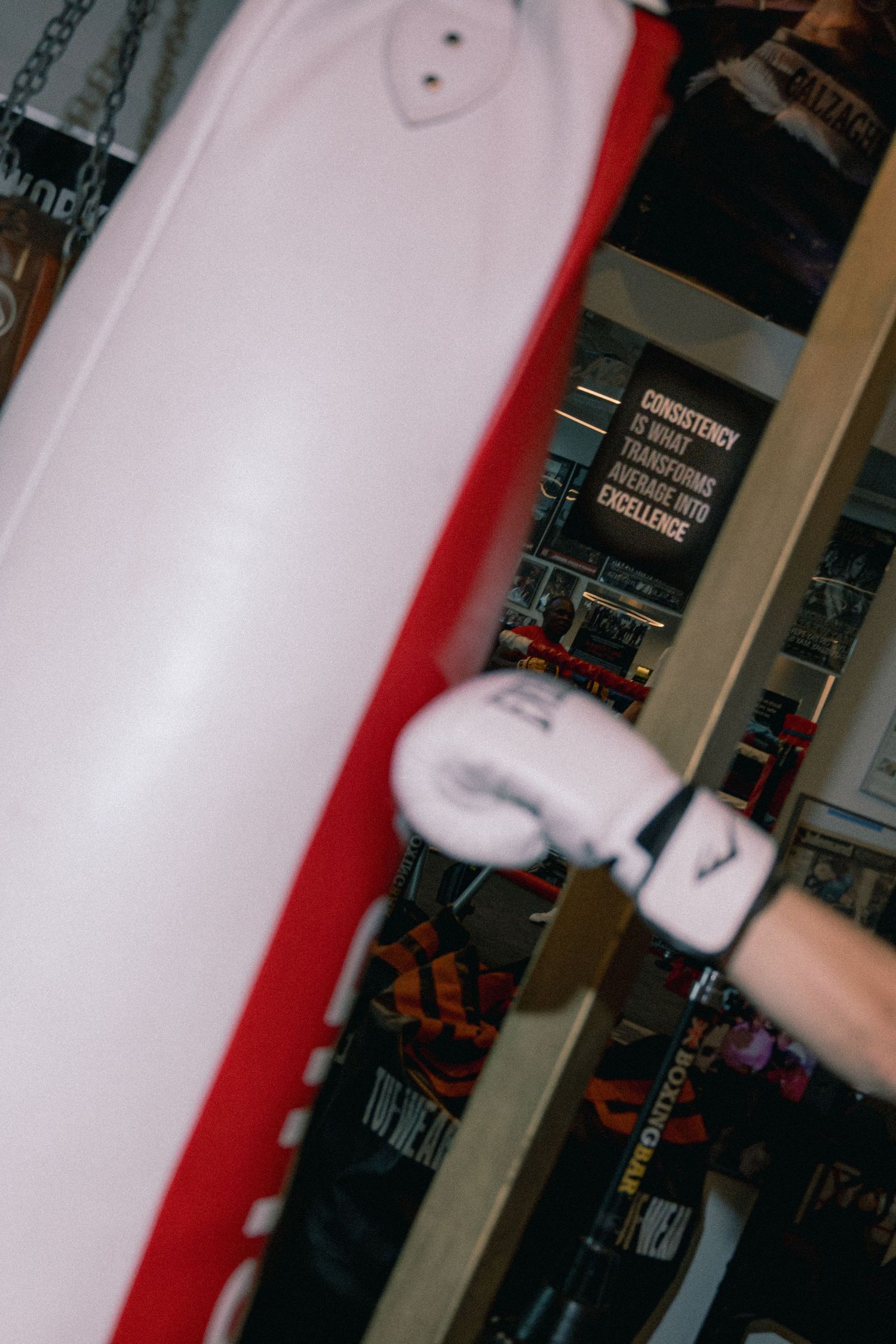 Boxer in white gloves training on a red and white punching bag in a gym with motivational quote on wall.