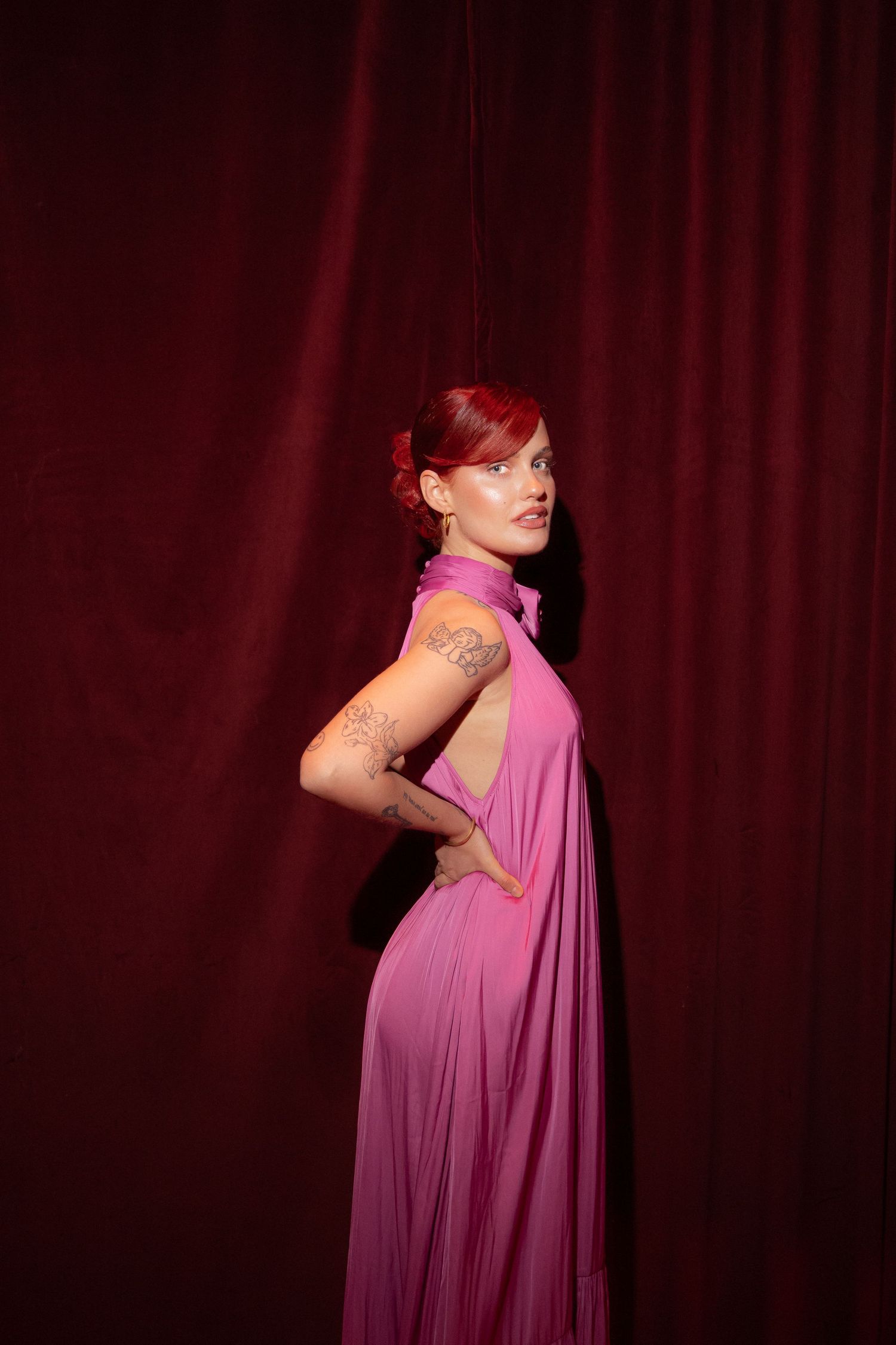 A model in a flowing purple gown poses dramatically against a deep red curtain backdrop.