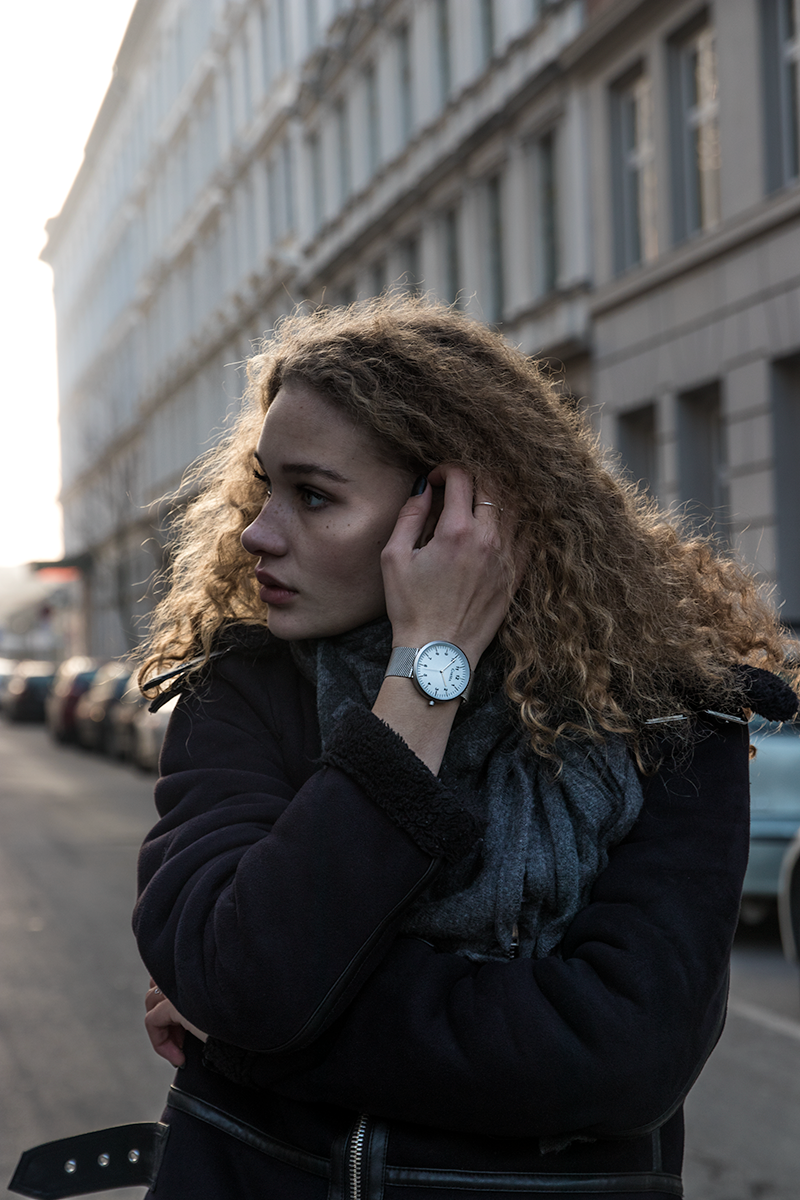 Person with curly hair looking through binoculars against urban backdrop.