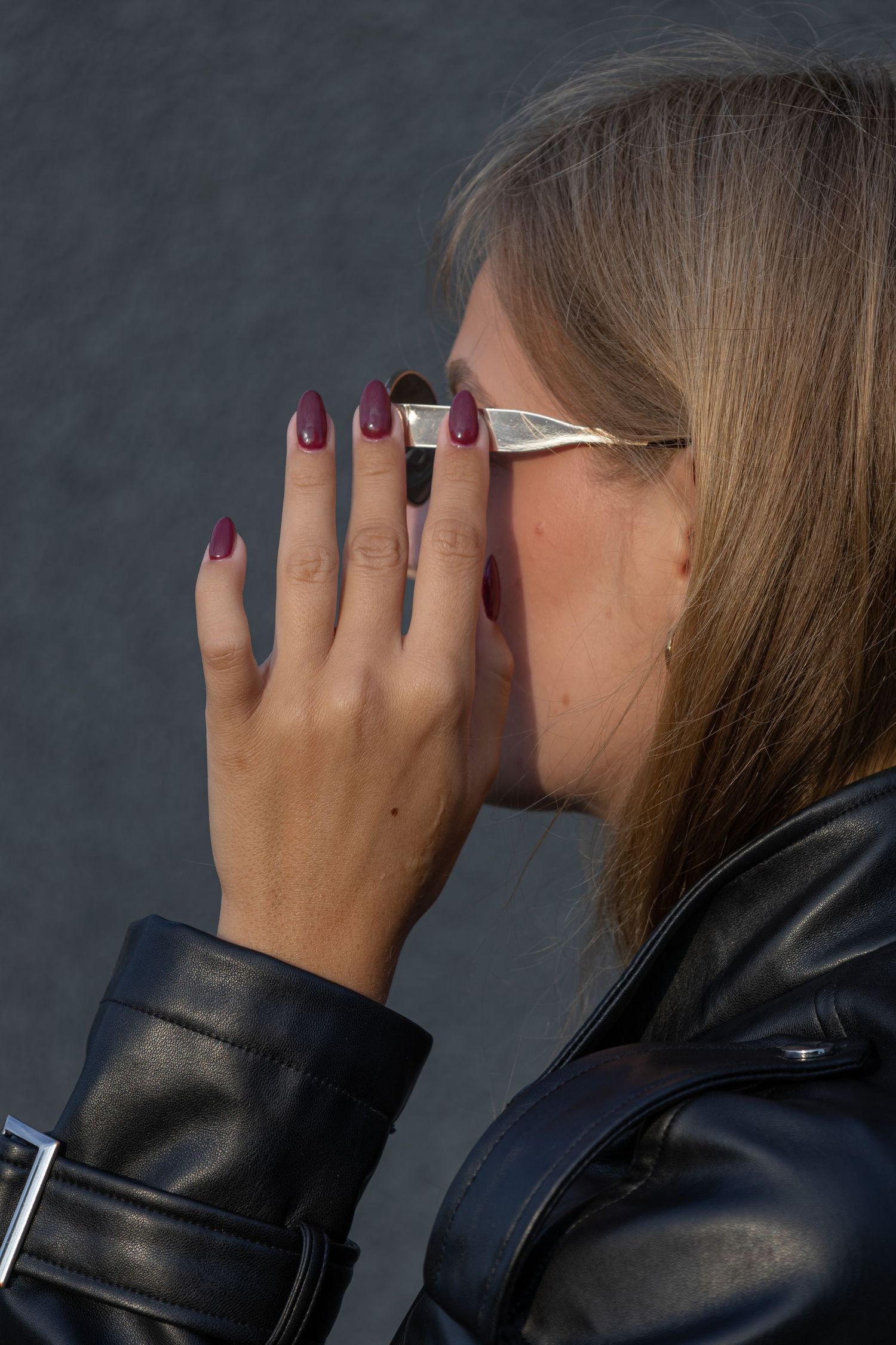 Side profile showing burgundy painted nails against dark background.