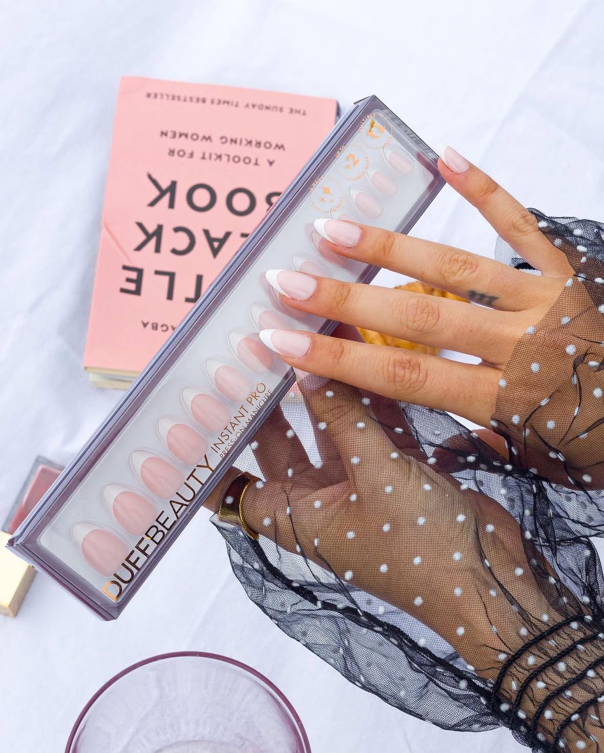 Hand with polka dot sleeve holding pink beauty product packaging.