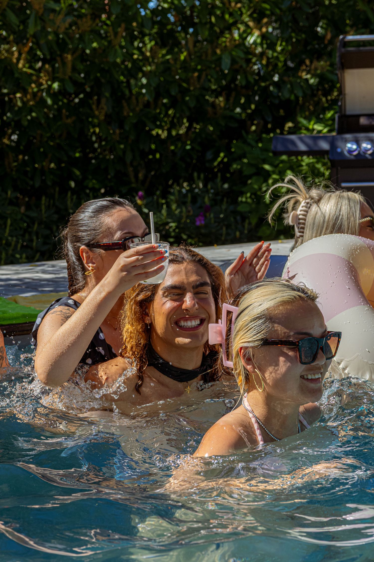 Group of women laughing and splashing in a outdoor swimming pool on a sunny day.