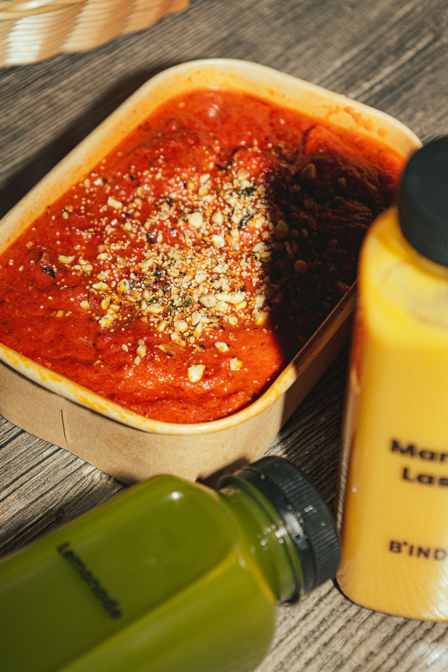 Sprinkling dried herbs and seasonings onto a red tomato sauce spread across a wooden surface.
