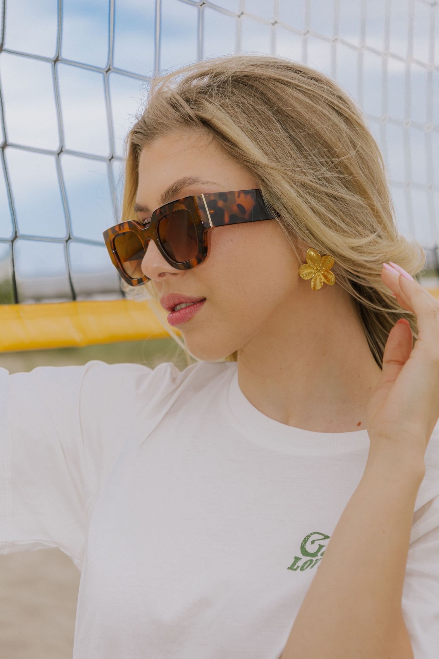 Profile view of person in white t-shirt and tortoise sunglasses against volleyball net.