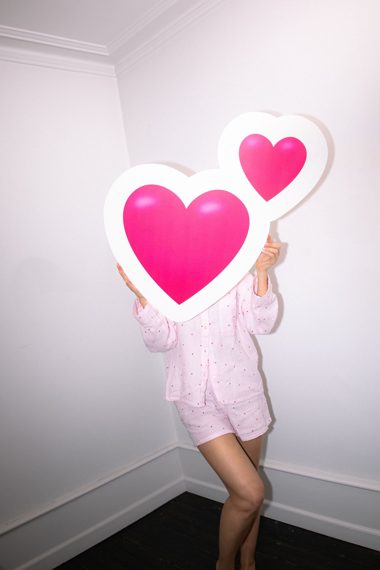 Person in pink sleepwear holding large heart-shaped sign against white wall in sequence of four similar poses.