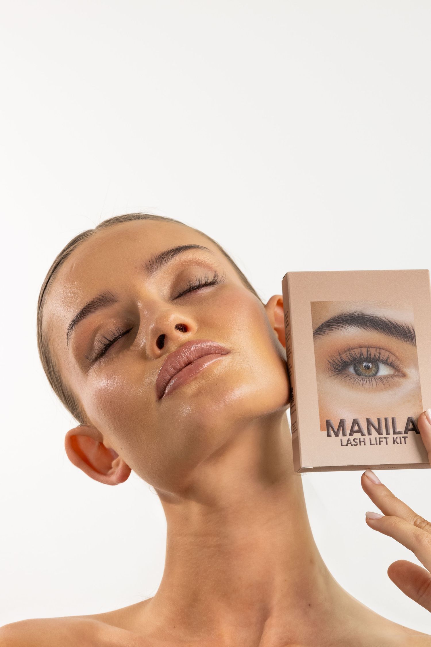 Model holds Manila Lash Lift Kit box against her cheek, showcasing glowing skin and natural beauty.