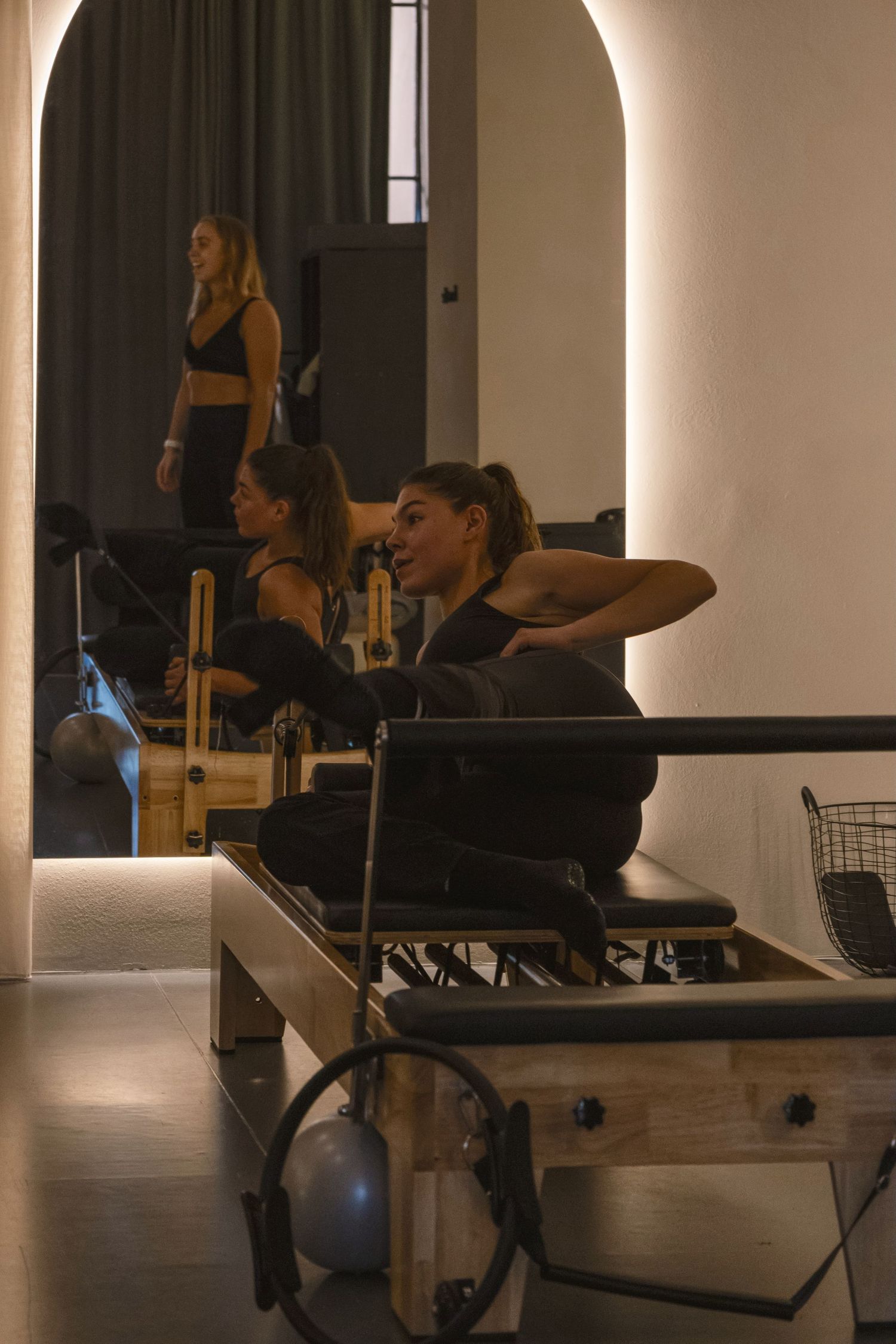 Women exercising on Pilates reformer machines in a modern, warmly lit studio during a group fitness class.