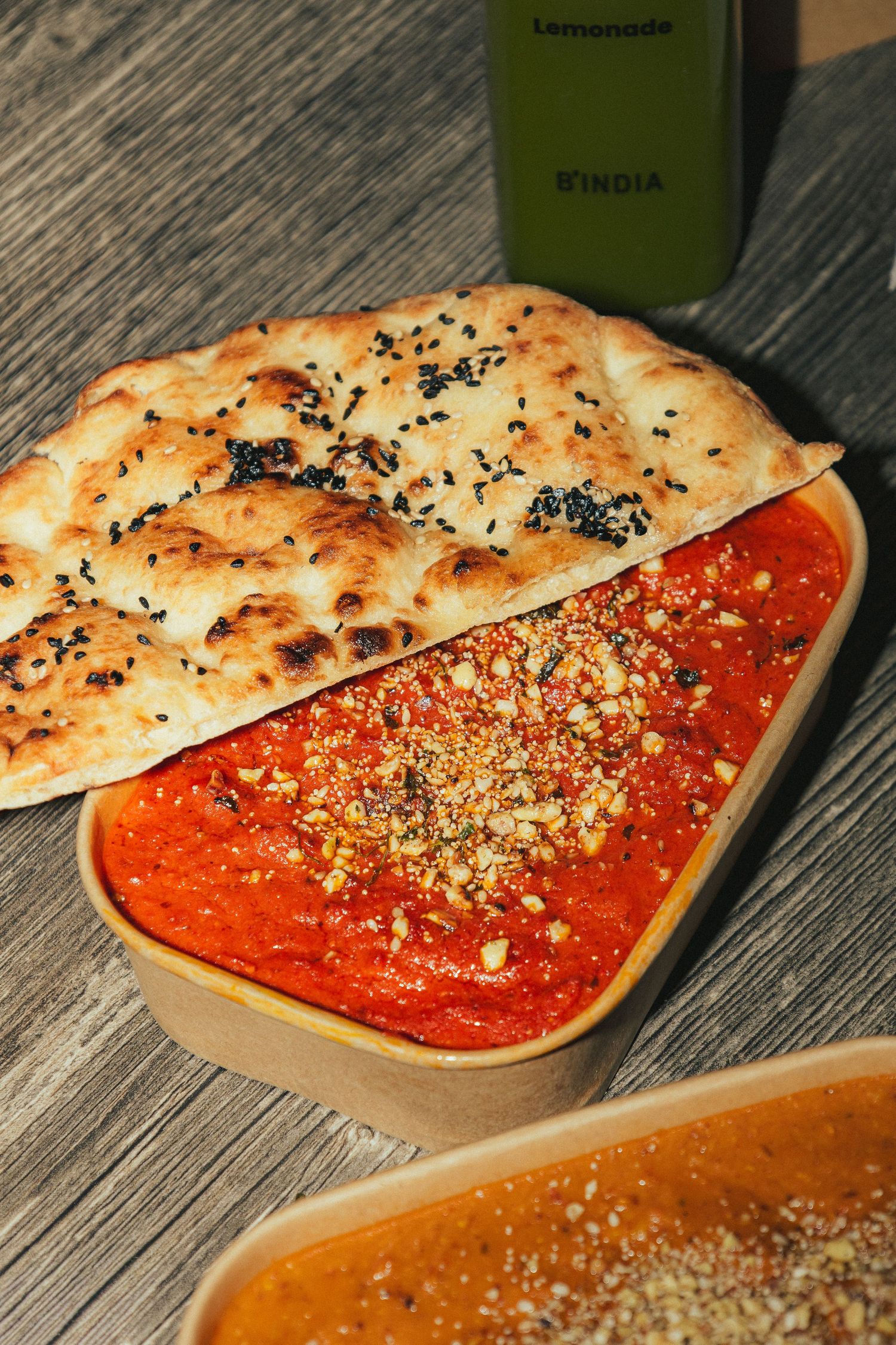 Flatbread with black sesame seeds served alongside vibrant red tomato dip garnished with crushed nuts.