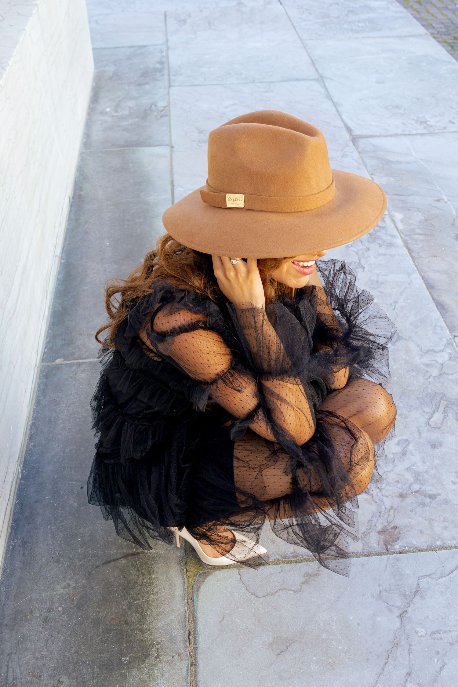 Stylish sequence featuring a tan hat and black tulle dress on stone flooring.
