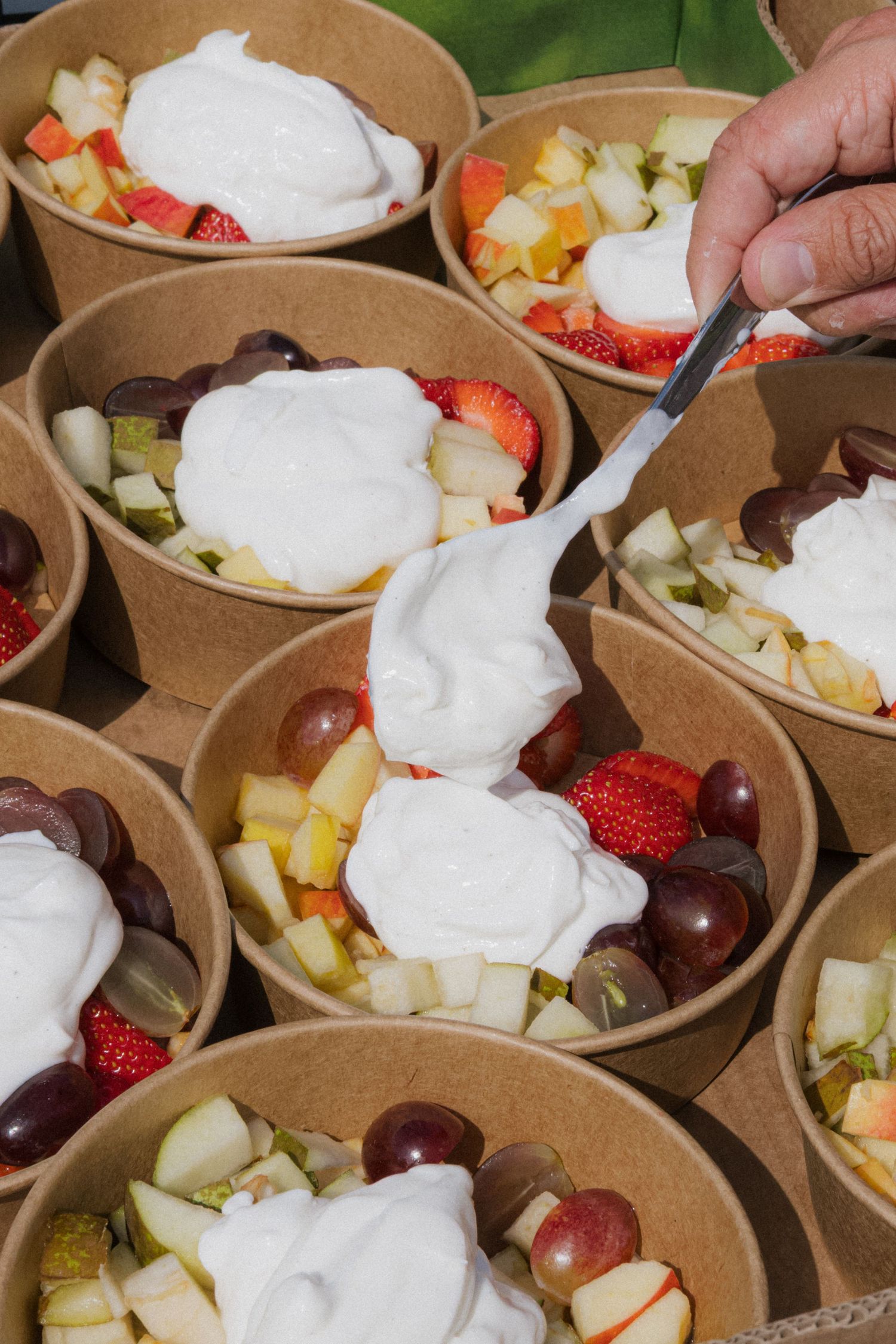 Fresh fruit bowls with whipped cream and strawberries in eco-friendly paper containers.
