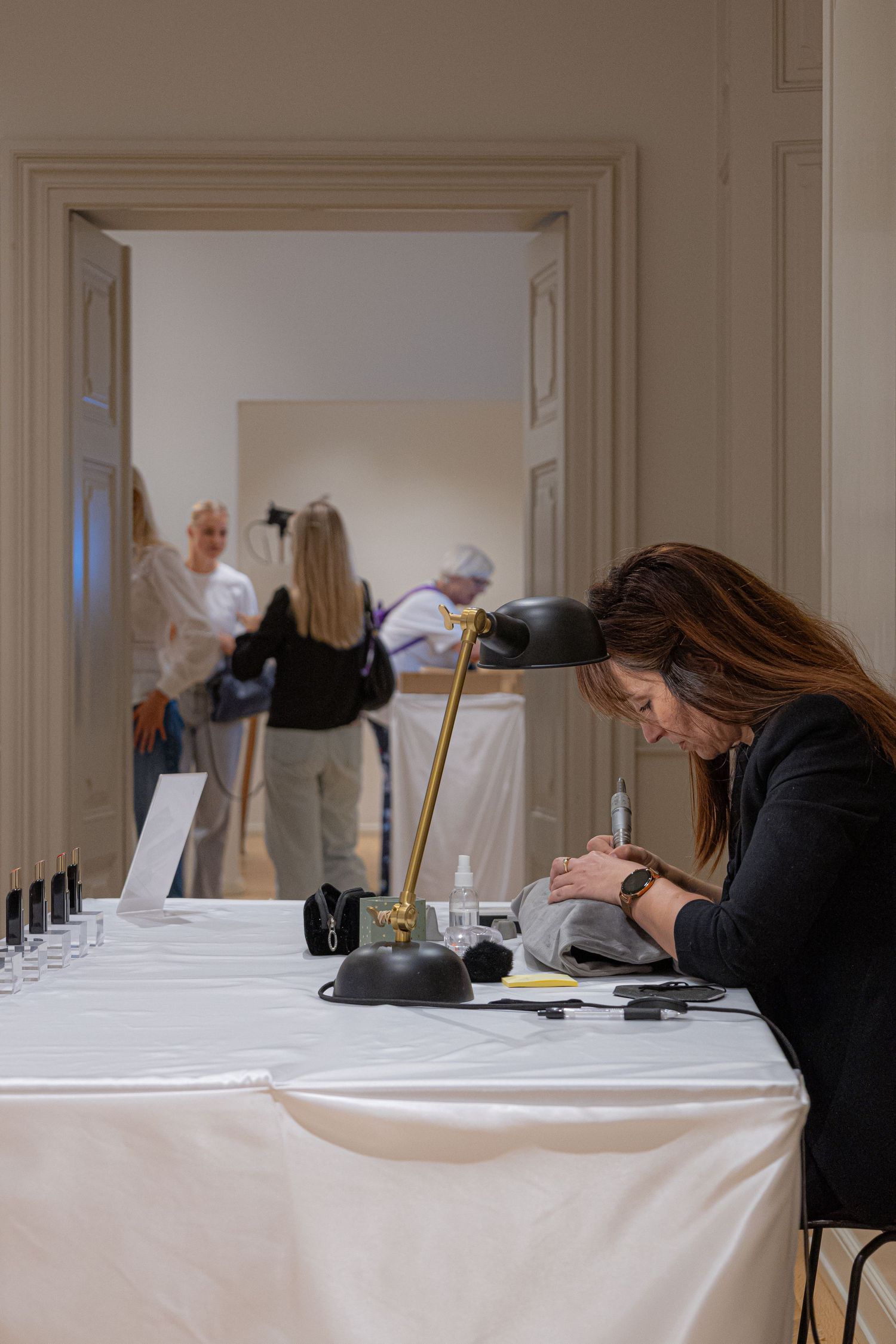 People working at tables covered in white tablecloths in an elegant room with high ceilings.