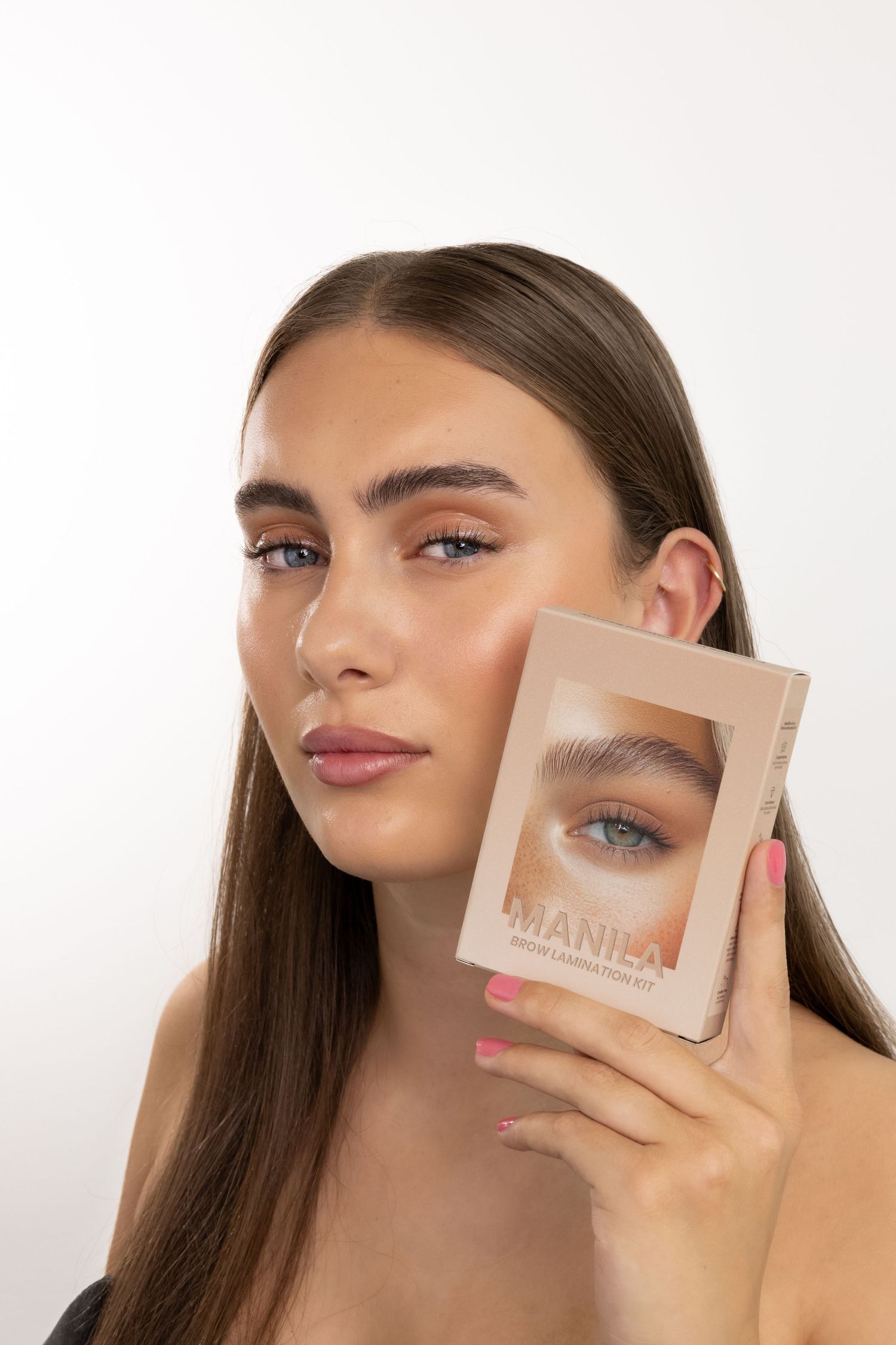 Young woman holding Manila Photo Correction Kit makeup palette next to her face against white background.