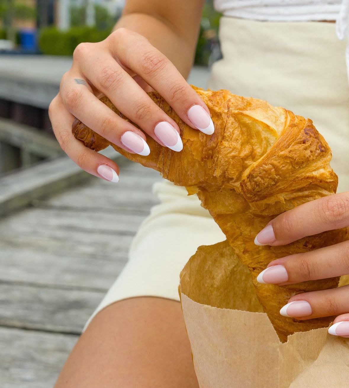 Hands with pink manicure holding a fresh golden croissant pastry.