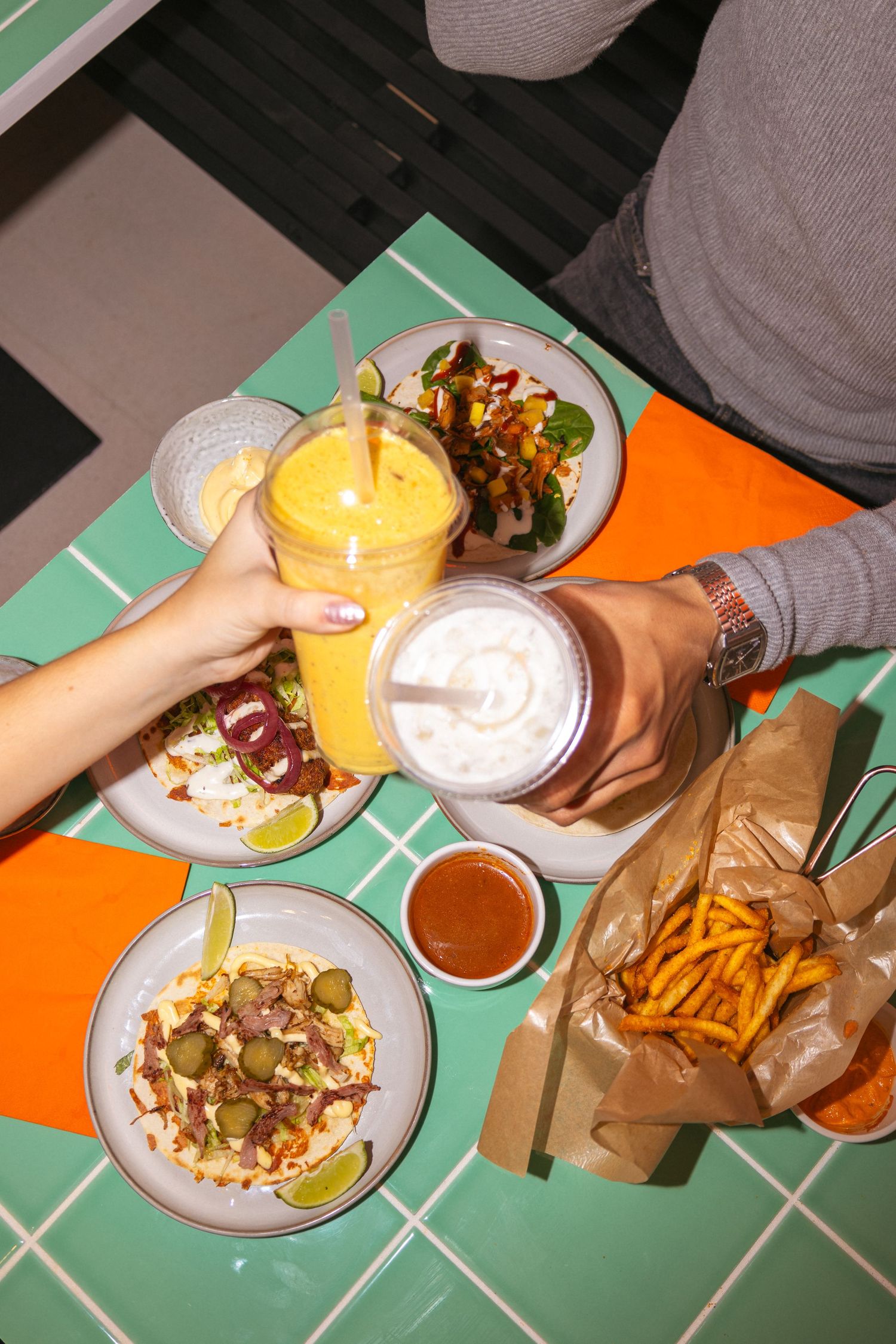 Overhead view of fast food meal with drinks and fries on turquoise table.