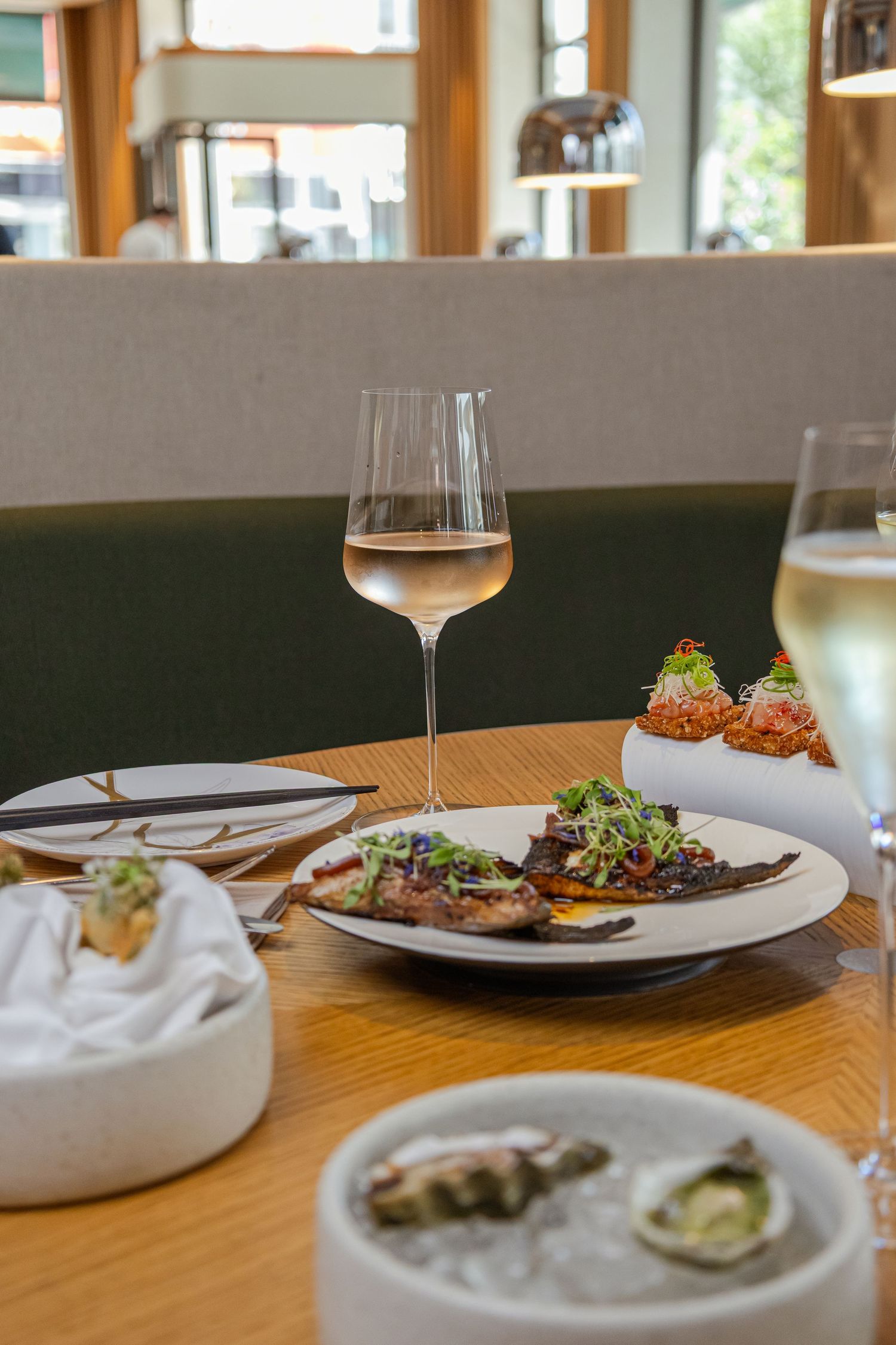 Elegant restaurant table with white wine, grilled fish, oysters, and gourmet appetizers in a modern dining setting.