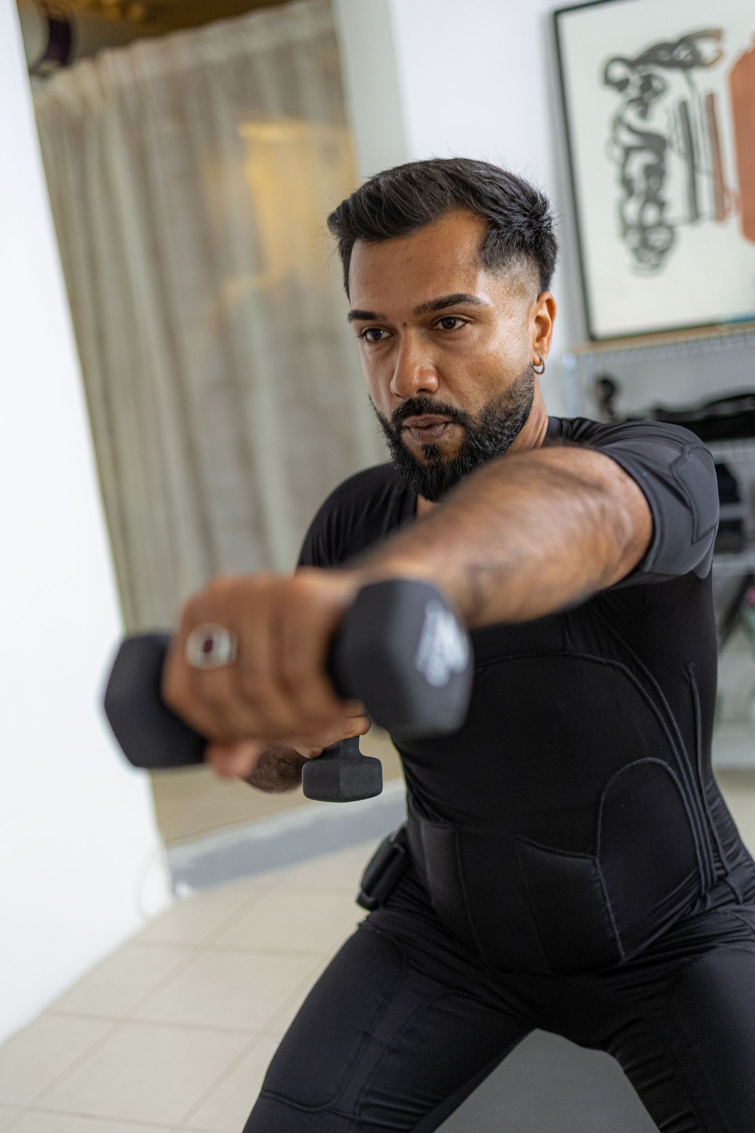 Fit man in black compression shirt doing dumbbell front raise exercise in home gym setting.