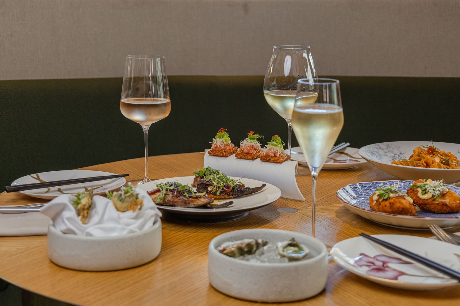 Elegant restaurant table with white wine glasses, gourmet appetizers, and Asian-inspired dishes on a wooden table.