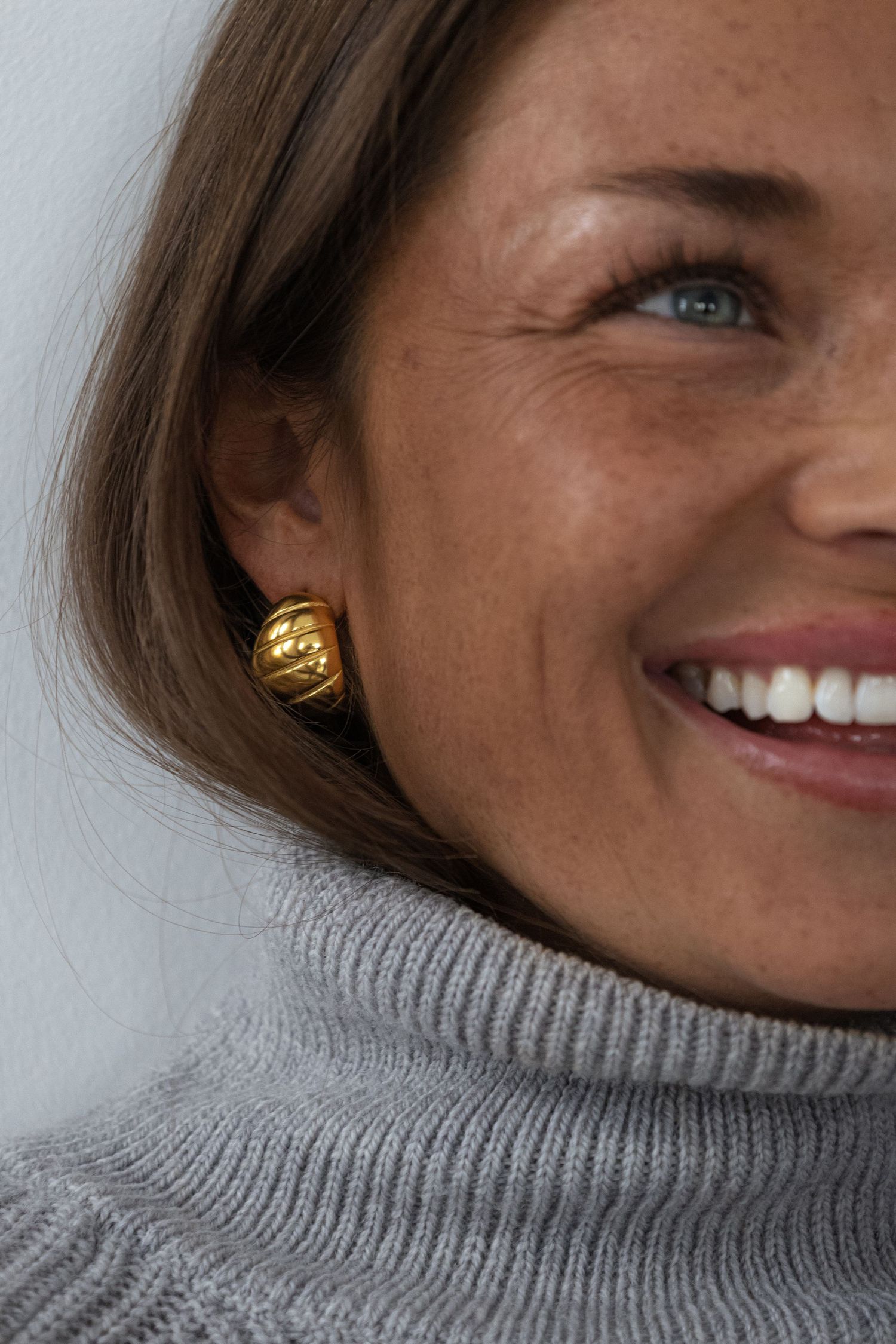 Close-up portraits showing gold earring and warm smile in grey turtleneck.