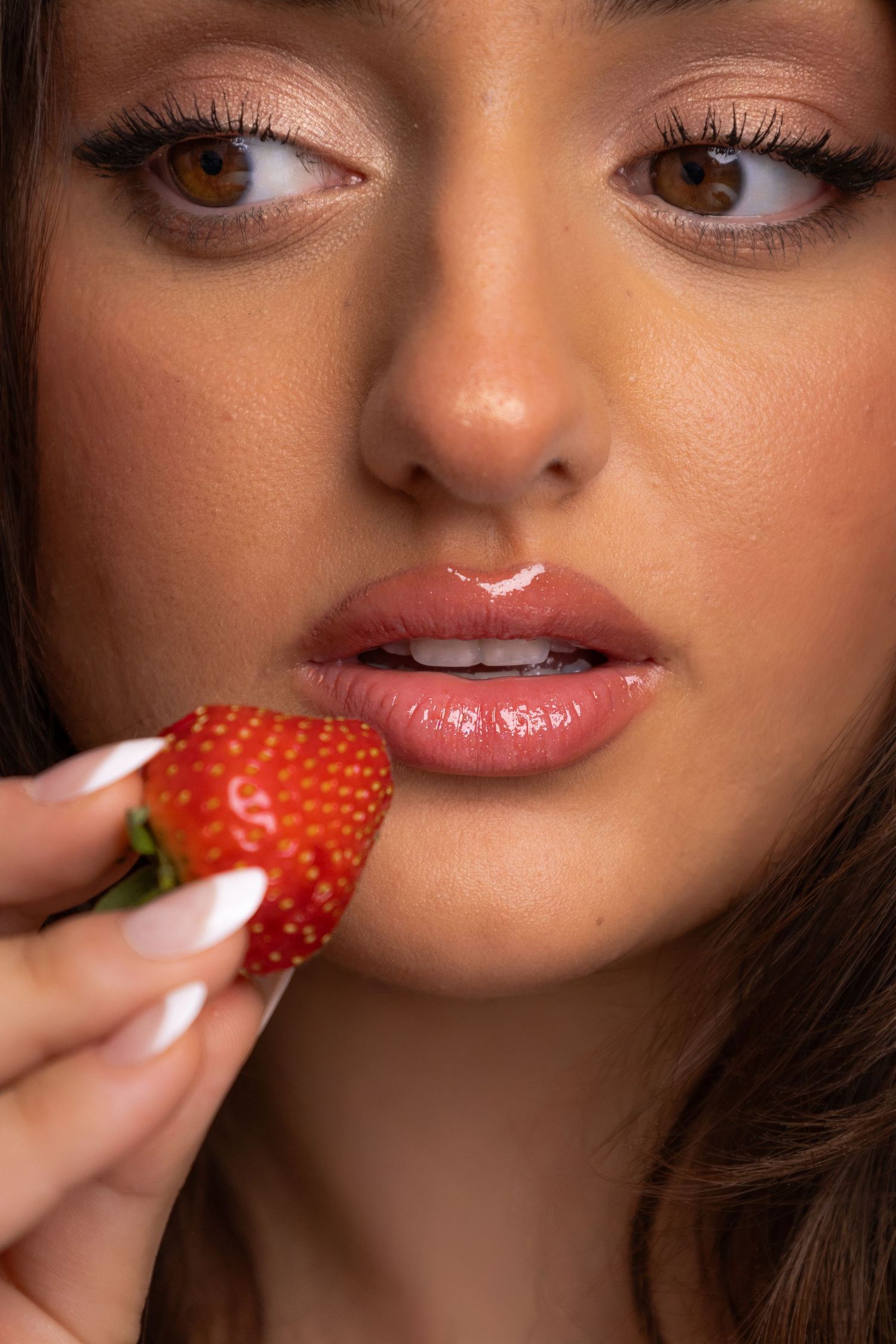 Close-up beauty shots with strawberry held near lips showing glamorous makeup details.
