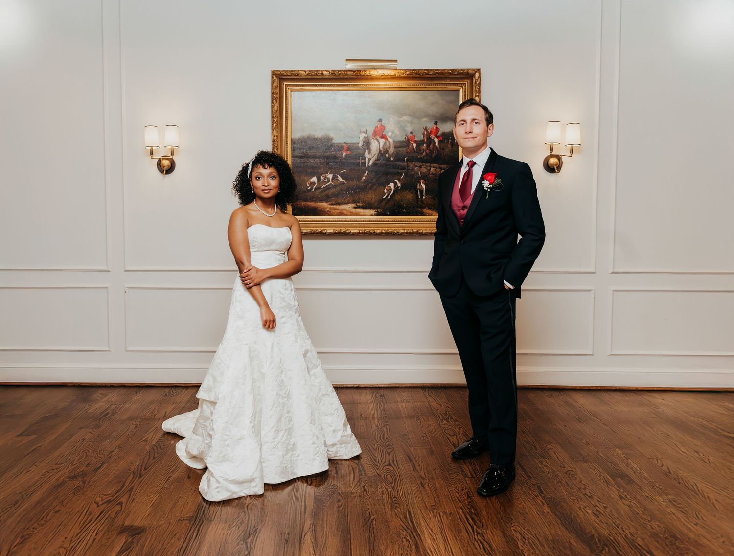 A formal wedding portrait in an elegant room with hardwood floors and classical artwork.
