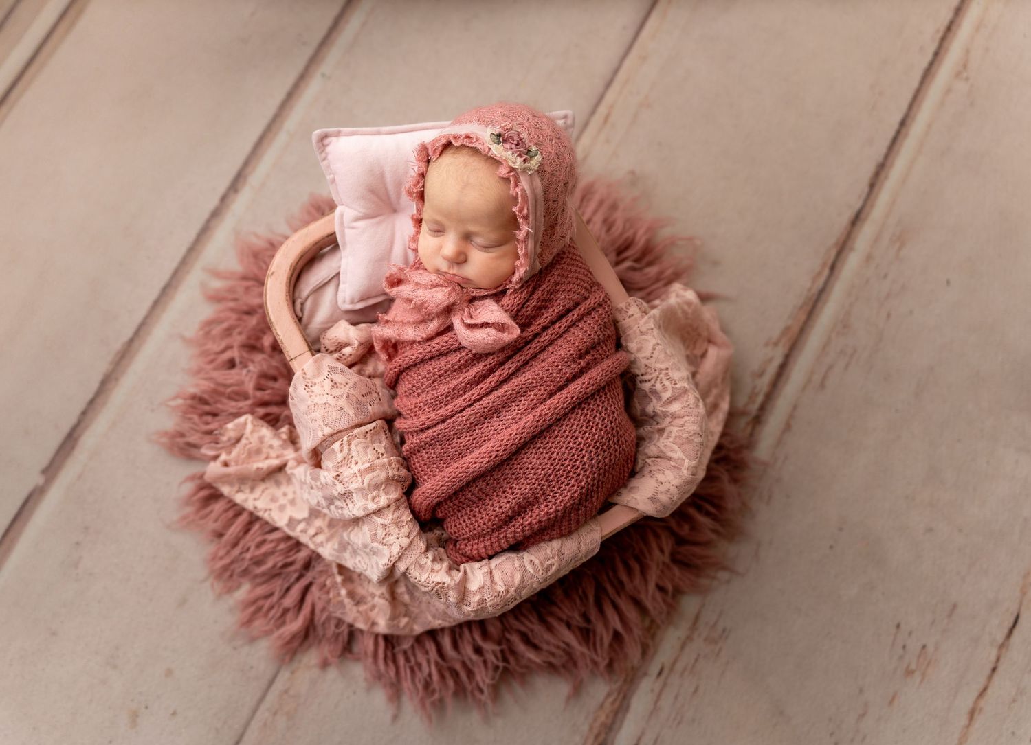 Sleeping newborn wrapped in dusty rose swaddle on textured blanket.