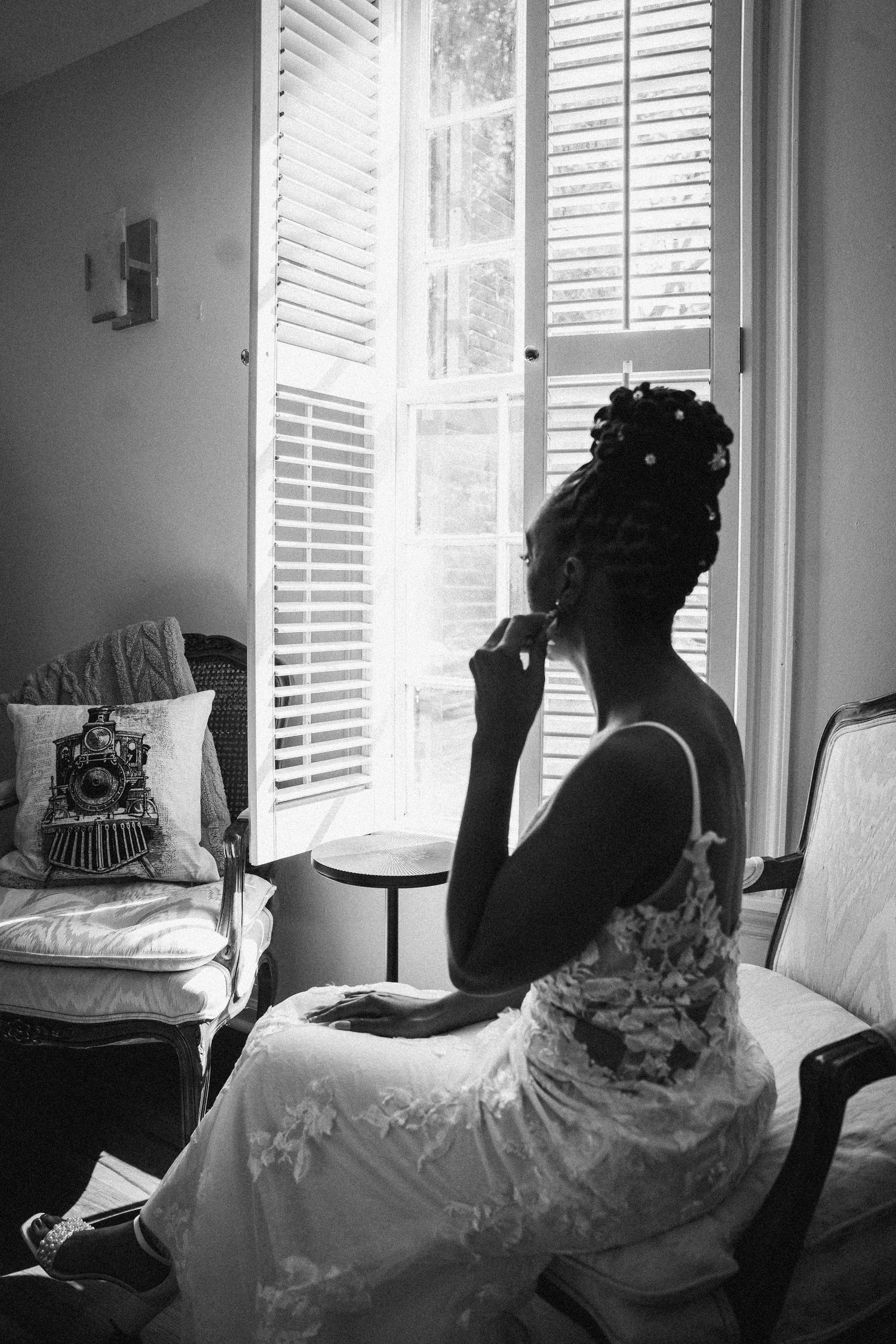 Silhouette of a bride in a wedding dress gazing through a window with plantation shutters.