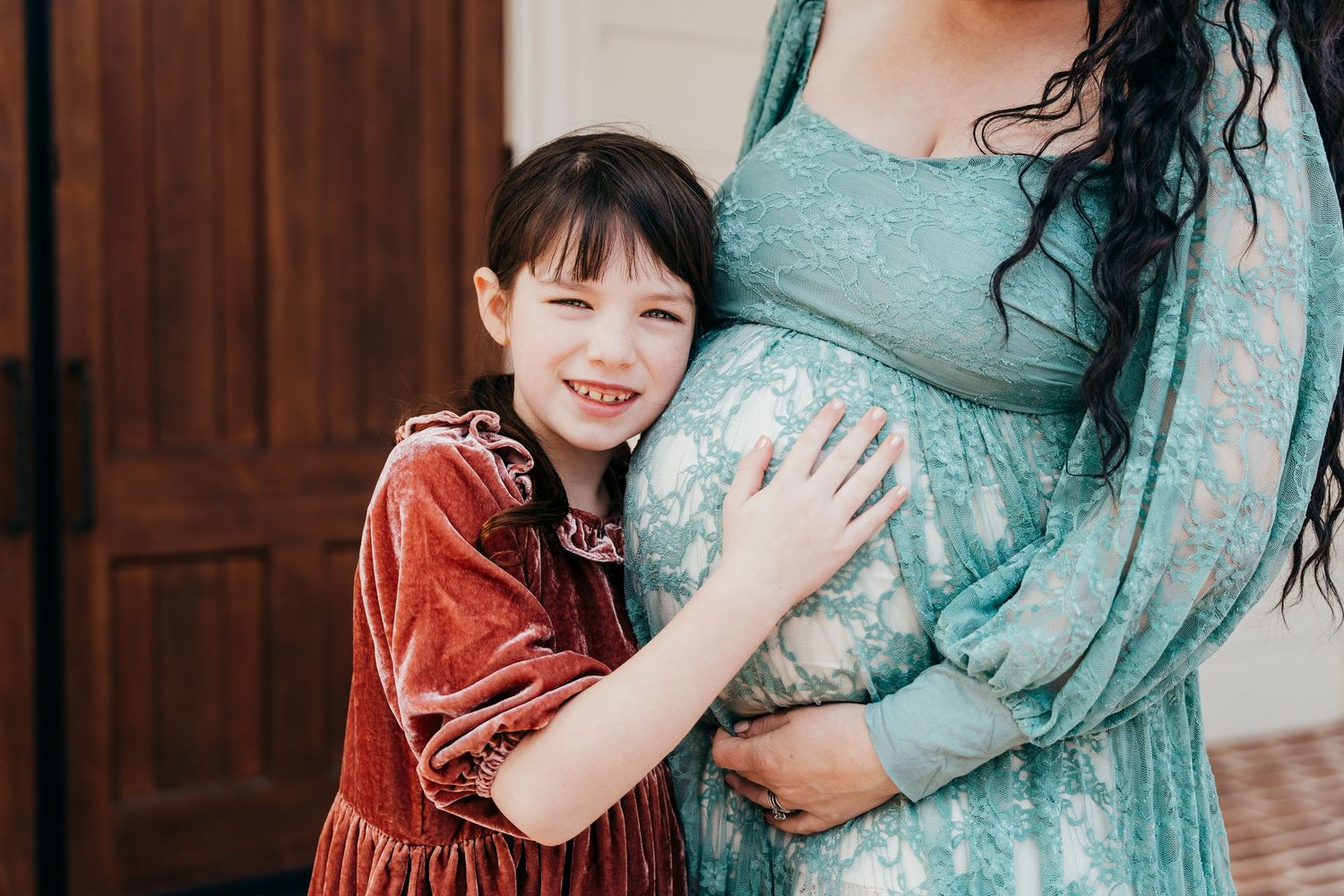 Maternity photo showing pregnant woman in teal dress with child hugging belly.