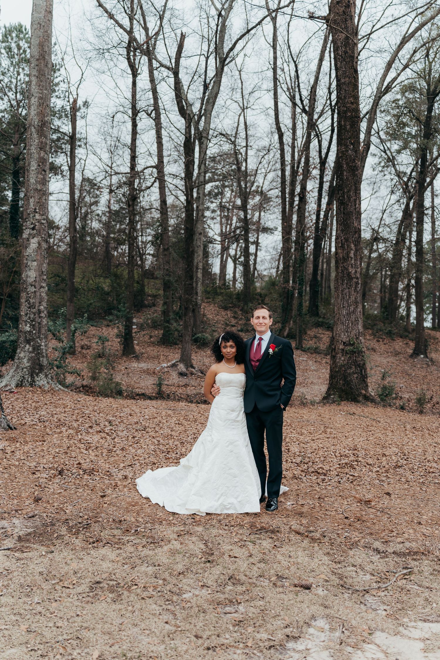 A wedding portrait in a serene wooded setting with bare trees.