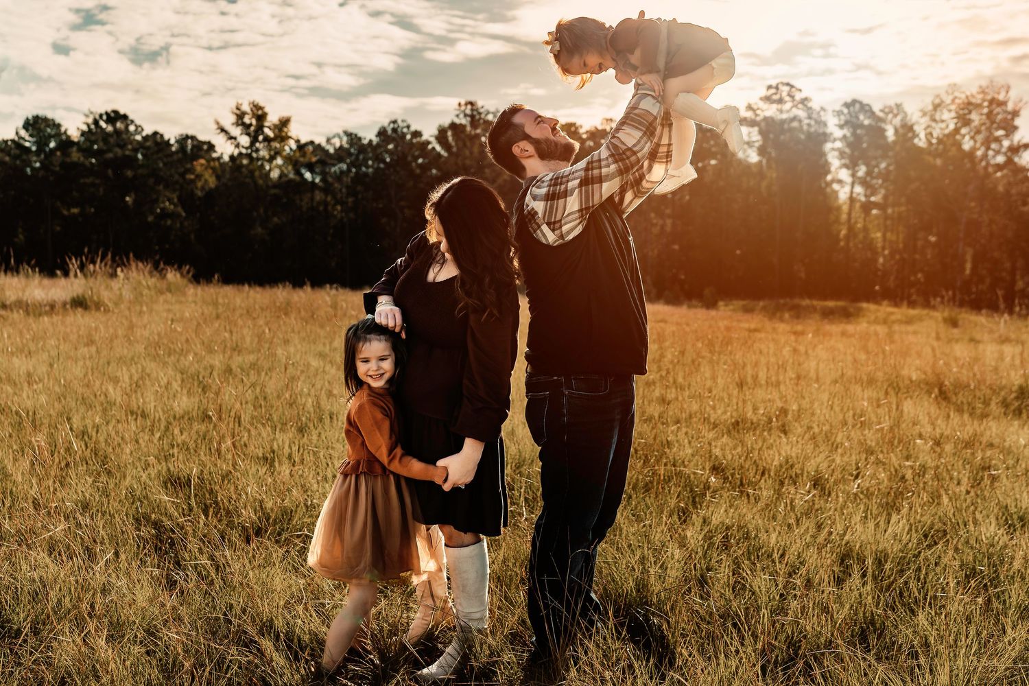 Family enjoying a playful moment together in a golden field at sunset.
