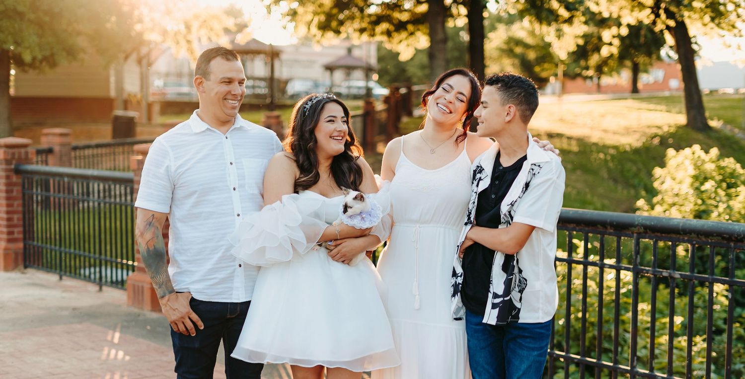 Group of friends in white outfits laugh together during outdoor photo session at sunset.