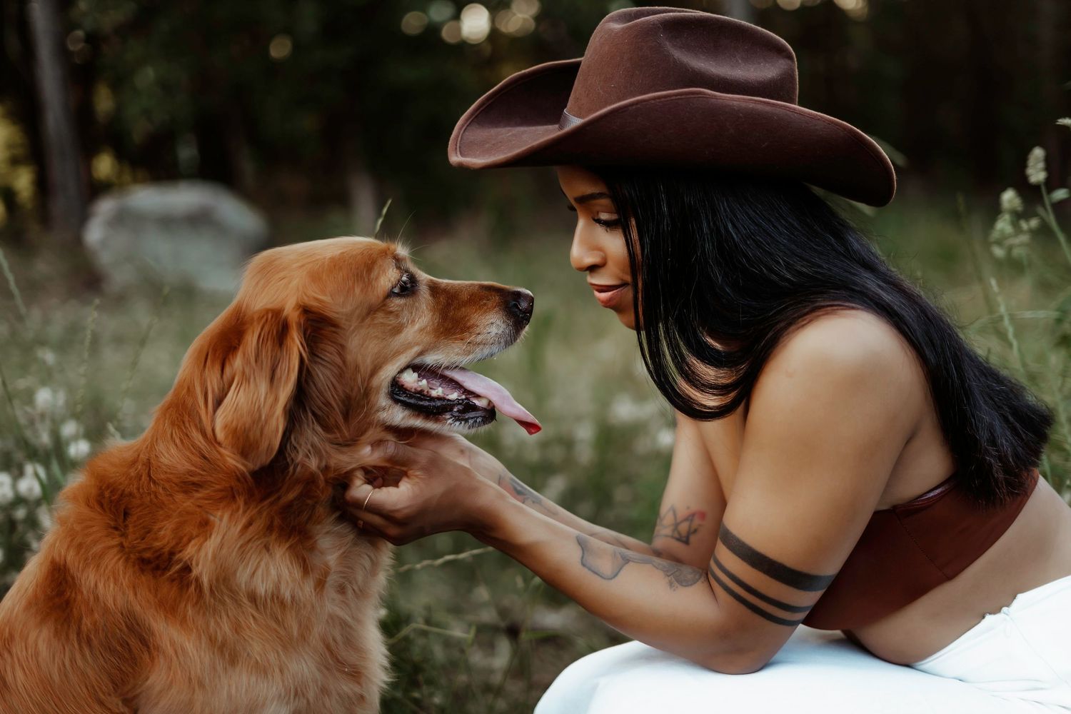 Woman in cowboy hat sharing tender moment with golden retriever dog in outdoor setting.