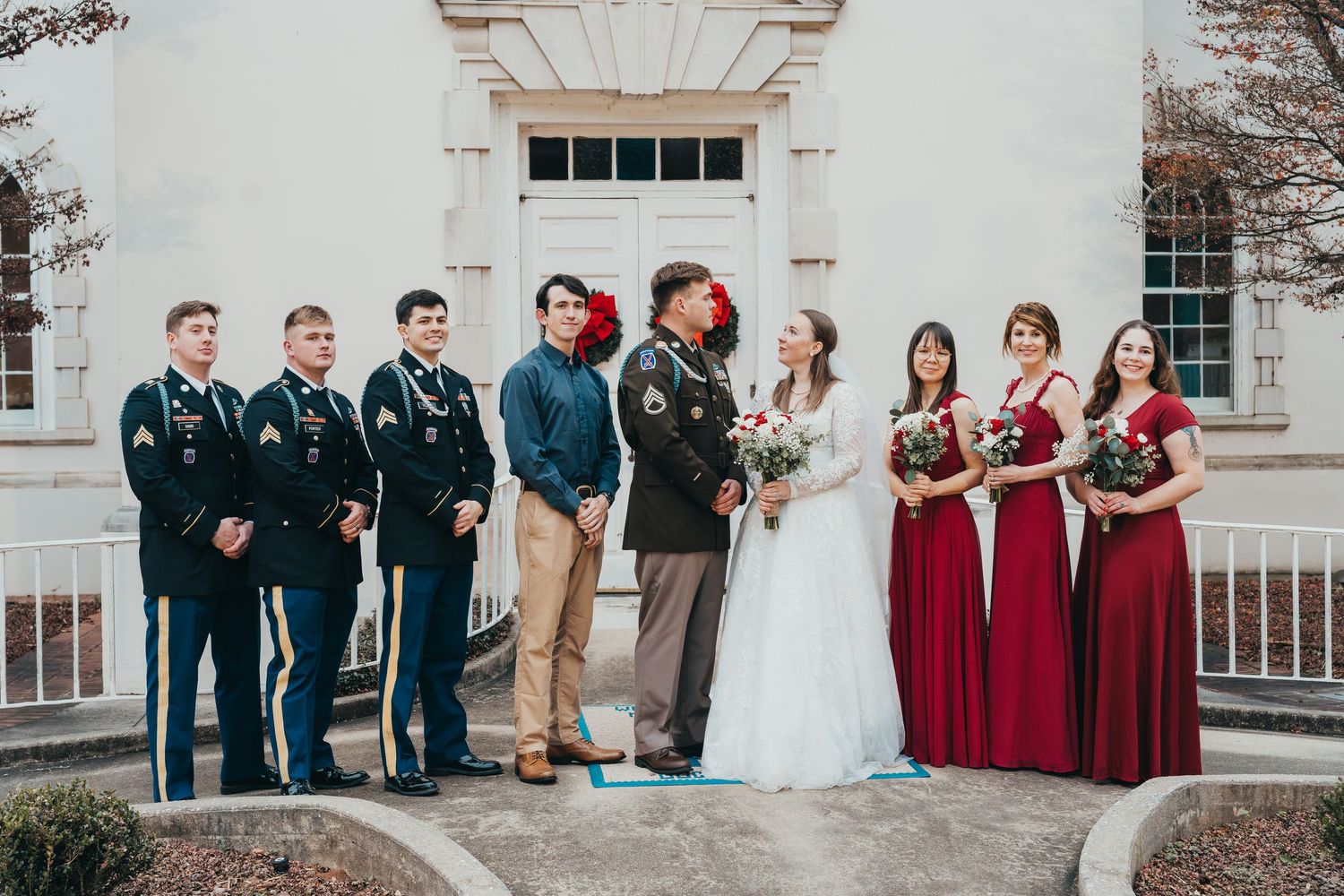 Military and wedding party formal group photo outside historic building with red and navy attire.