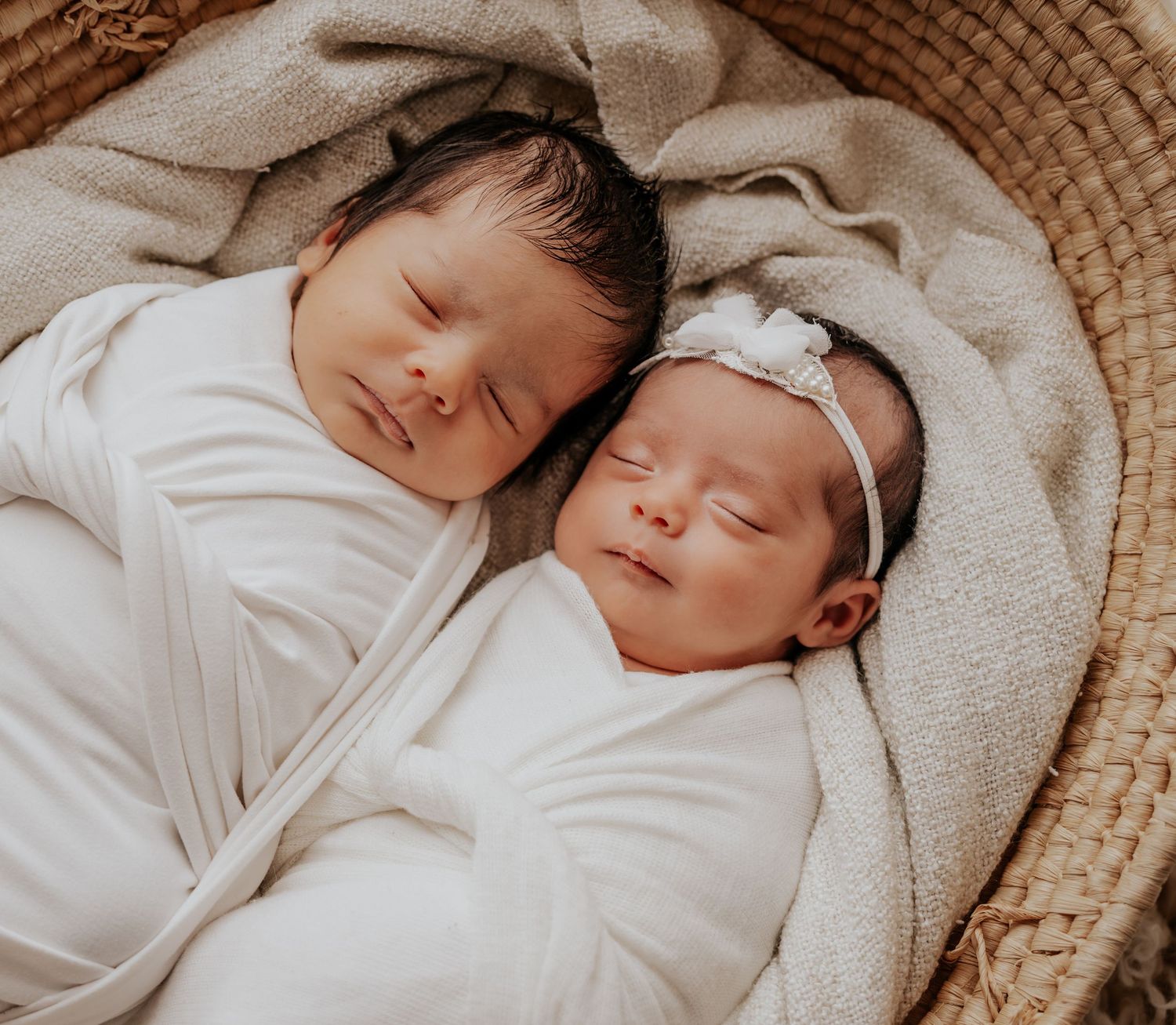 Two sleeping newborn babies swaddled in white blankets during professional photo session.