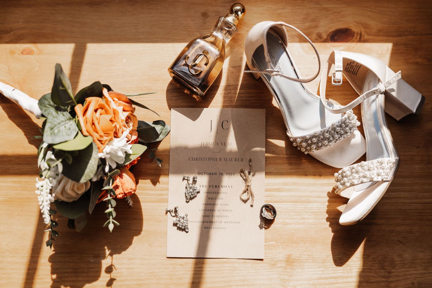 Wedding details flat lay with high heel shoes, bouquet, and wedding rings on wooden surface.