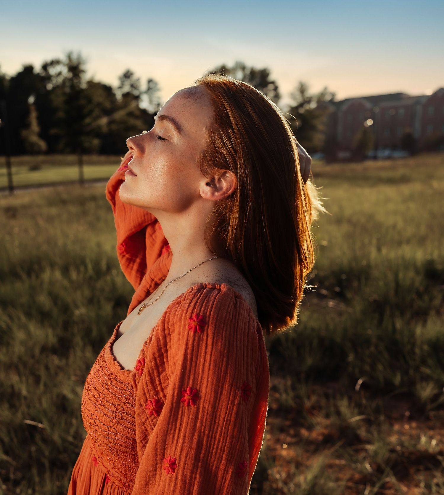 A woman in orange clothing tilts their head back in golden sunlight.