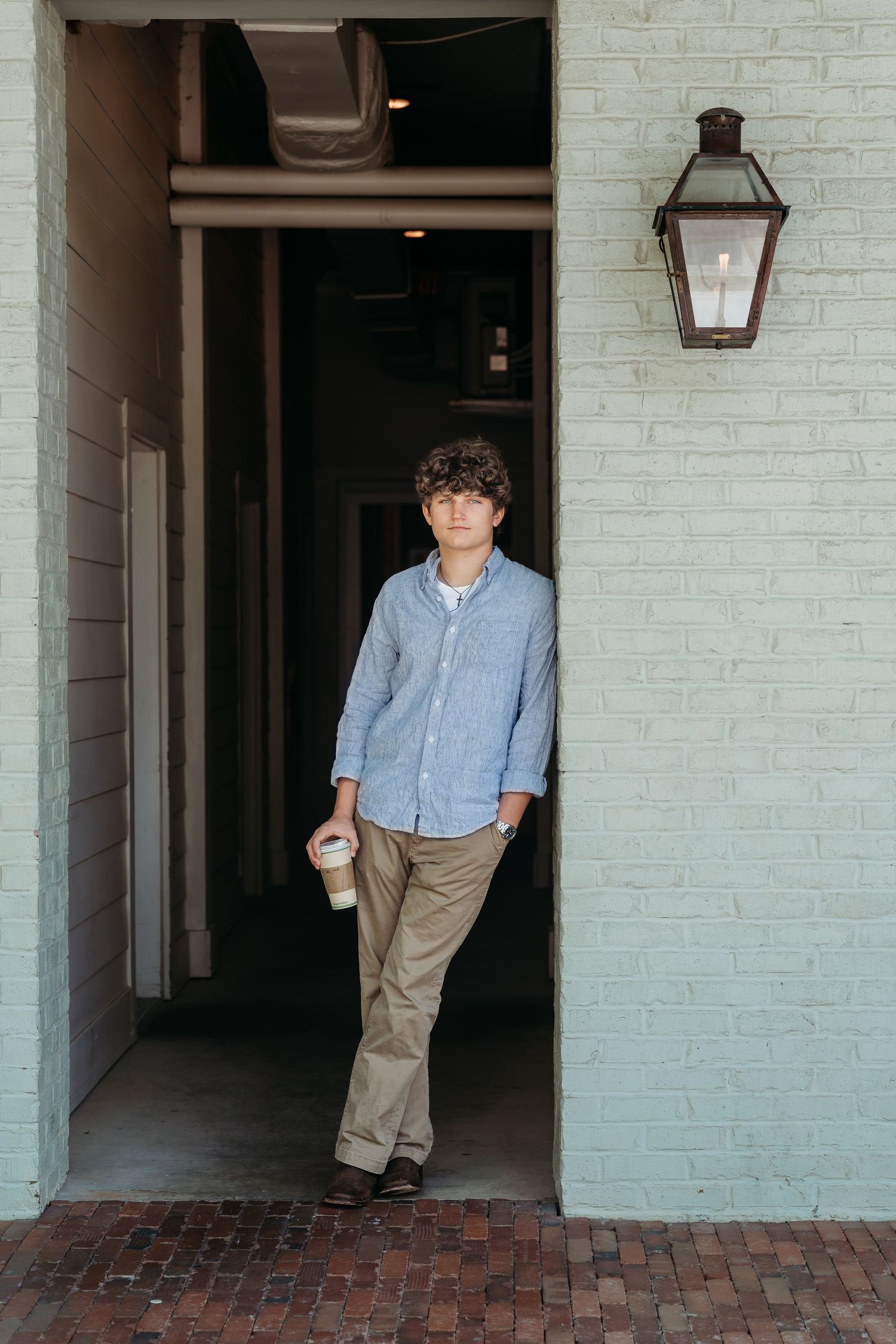 Casual portrait of person in blue button-down shirt standing in white brick doorway.