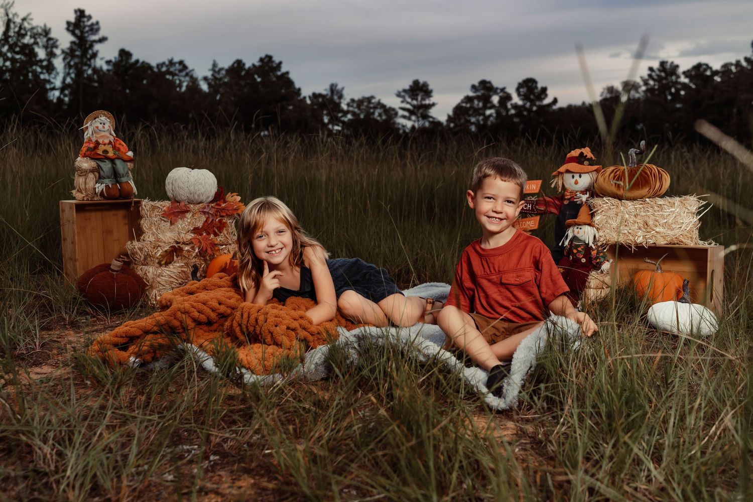Fall themed outdoor photo session with pumpkins and hay bales in rustic field setting.