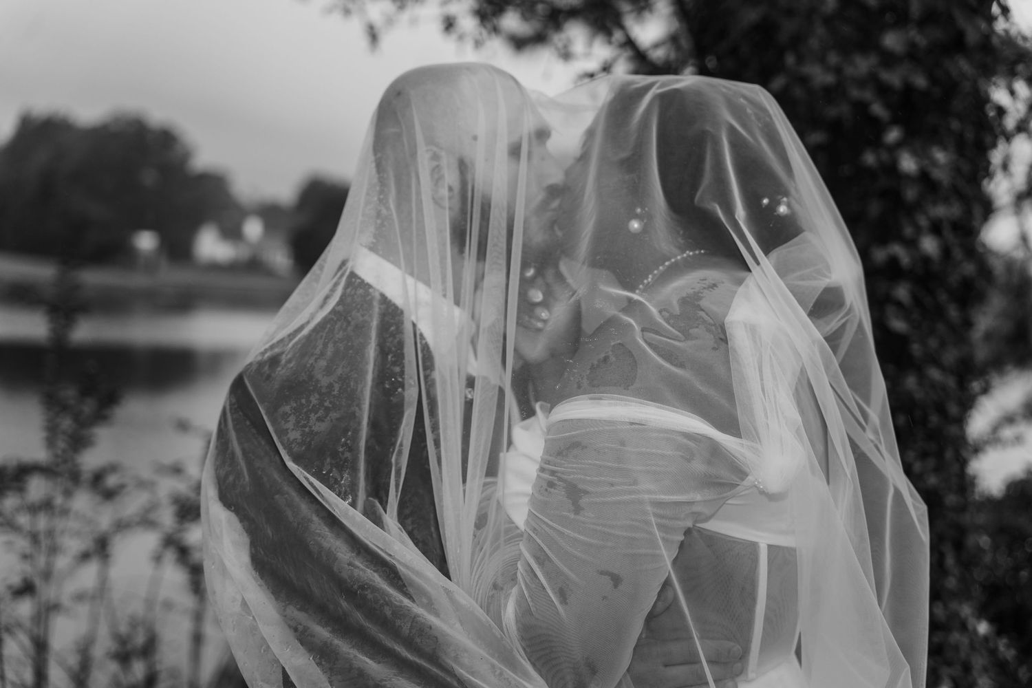 Black and white romantic photo of two figures sharing an intimate moment under delicate wedding veils.