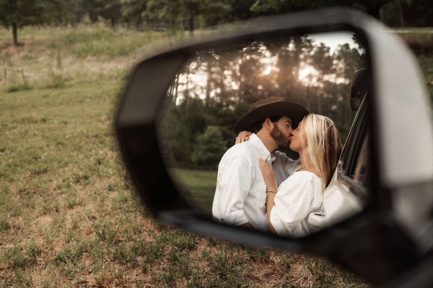 Romantic couple kissing captured through car side mirror reflection.