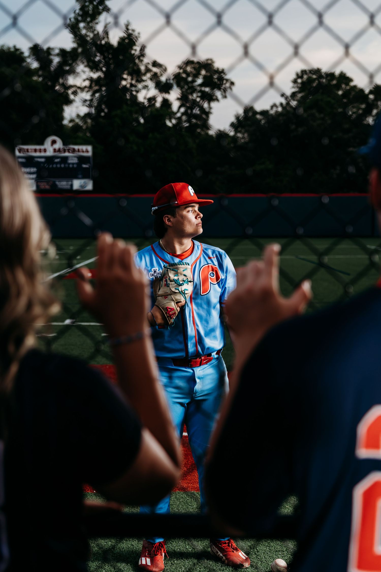 Baseball player in light blue uniform viewed through chain link fence during game.