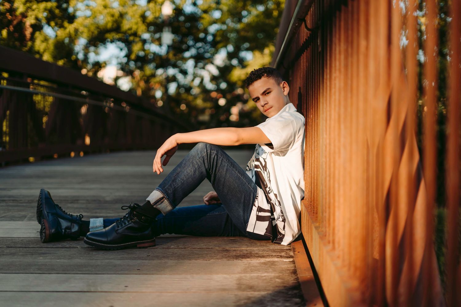 Person in casual attire sits alone against wooden wall in golden evening light.