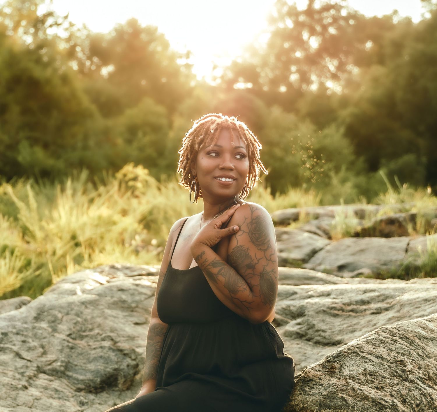 Candid sunset portrait of person with blonde locs sitting on rocky terrain.