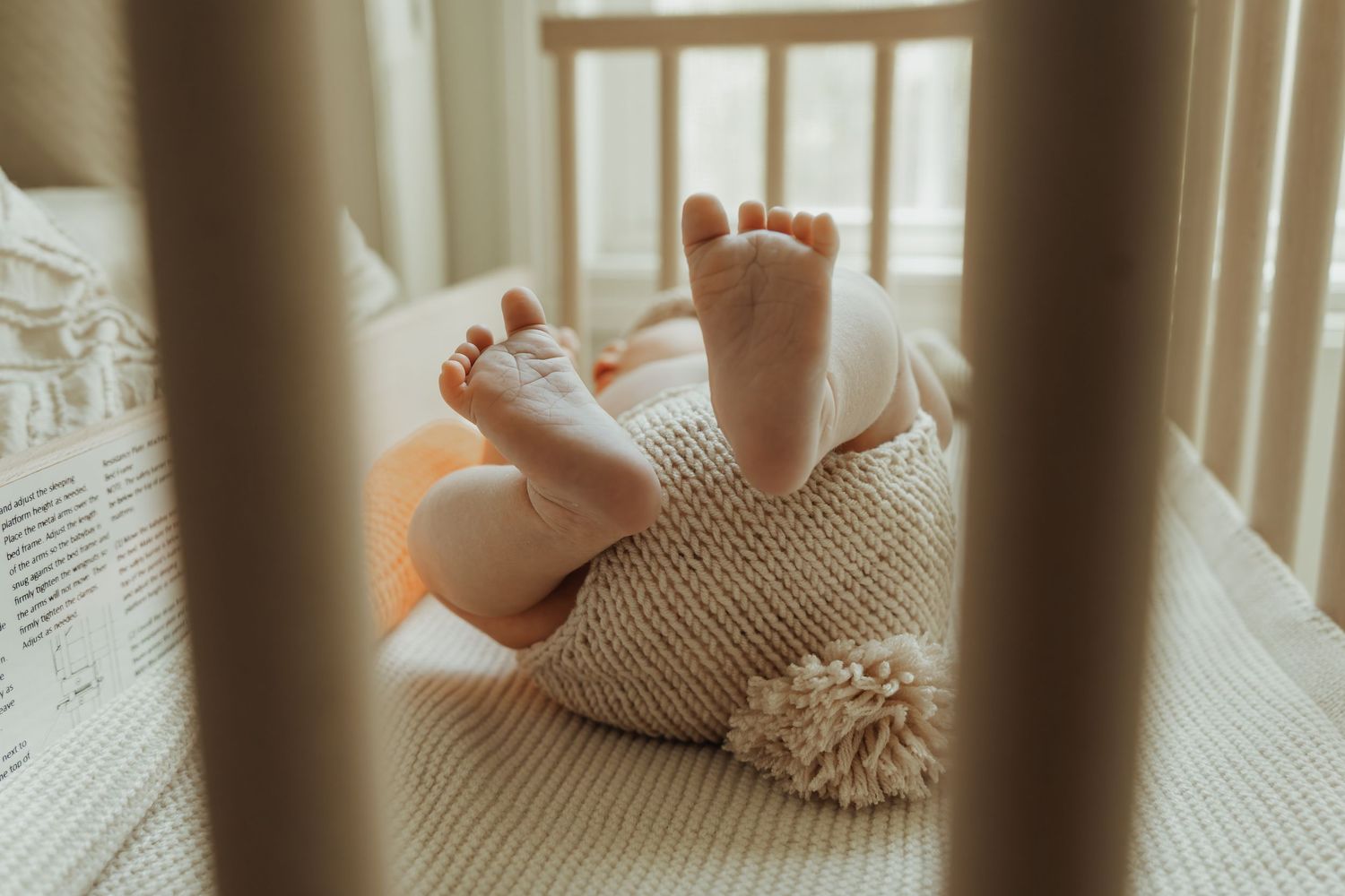 Baby feet peek through wooden crib rails in soft natural lighting.