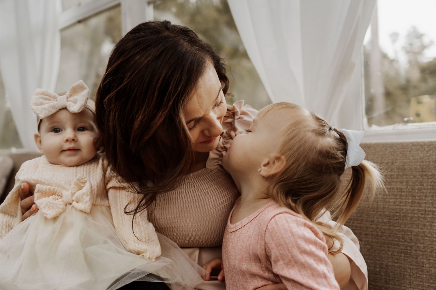 Parent and children share tender moment on couch in warm indoor setting.